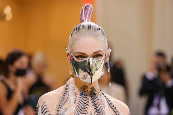 A closeup of Grimes on the red carpet wearing a metal face mask and long dangling ear cuffs