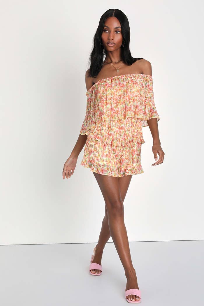 Model wearing tiered off the shoulder romper in peach floral pattern