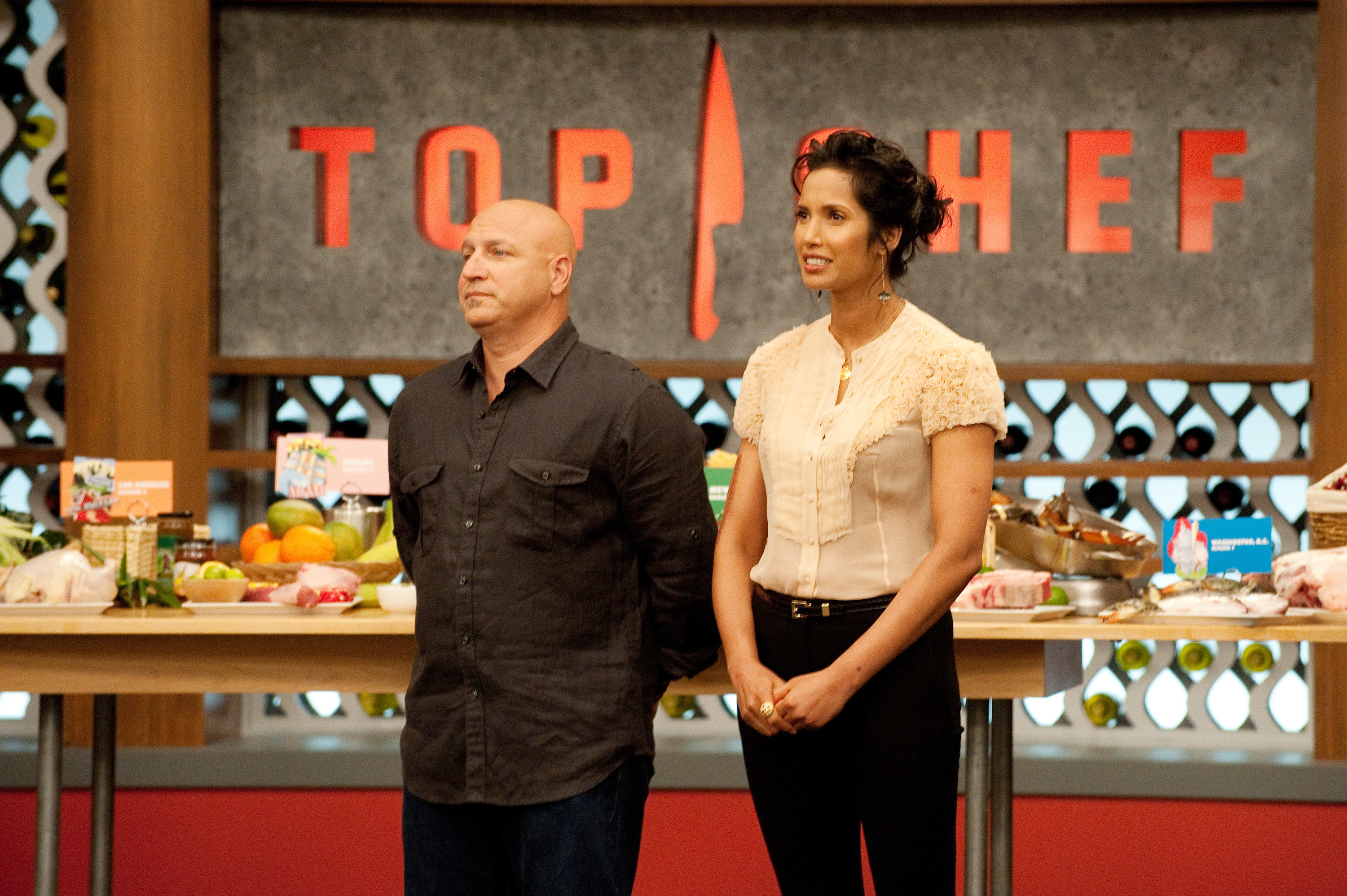 Tom and Padma stand next to each other in the Top Chef kitchen
