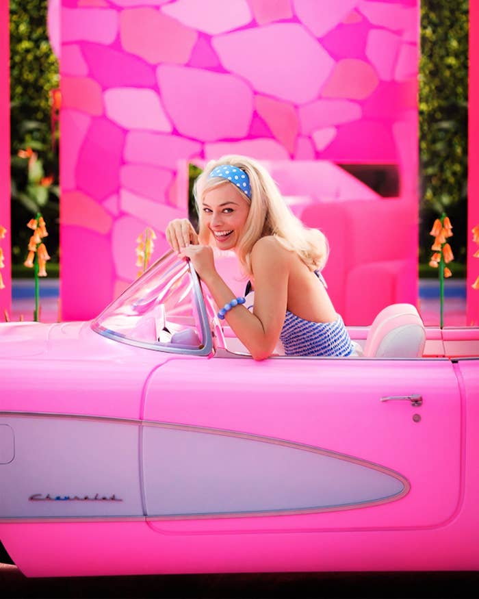 Margot Robbie as Barbie smiles as she sits in the driver&#x27;s seat of a pink convertible