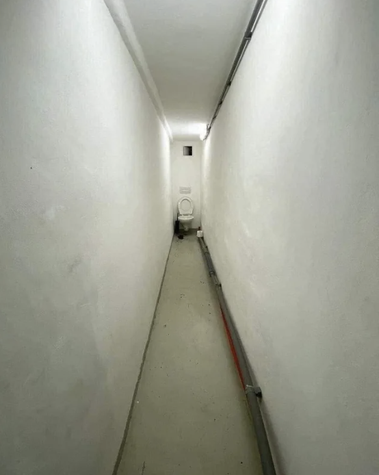 a long, narrow hallway with a toilet at the end