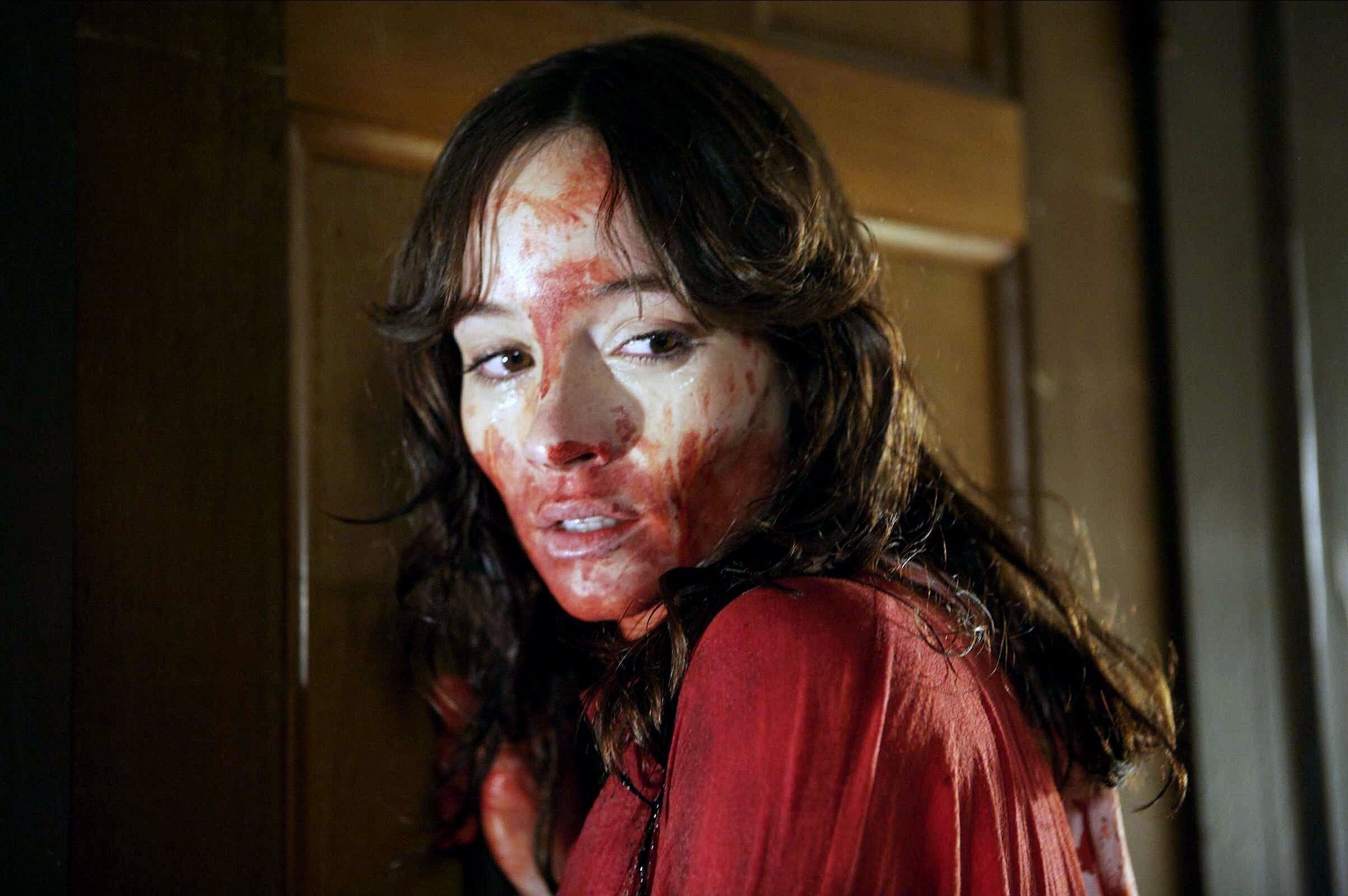 A blood covered woman leans against a large wooden door