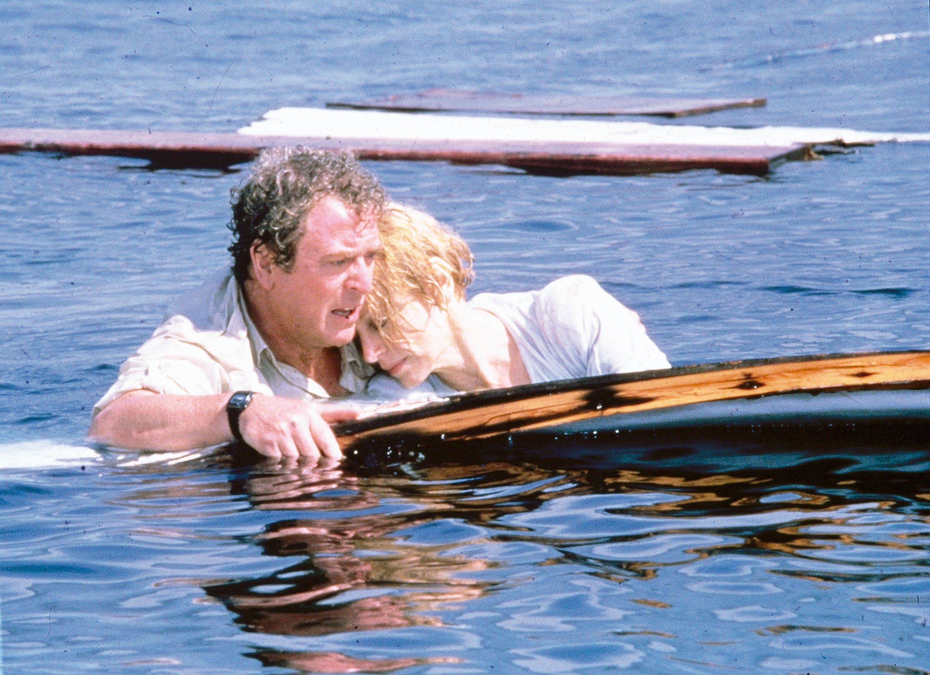 Michael Caine floats with a woman on boat wreckage in the Ocean