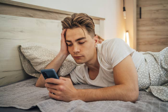 A man looks at his phone while lying in bed