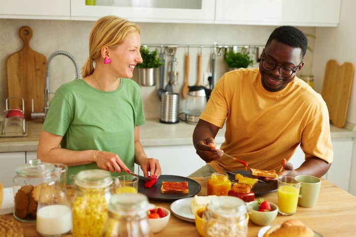 A couple laughs while eating breakfast together in their kitchen