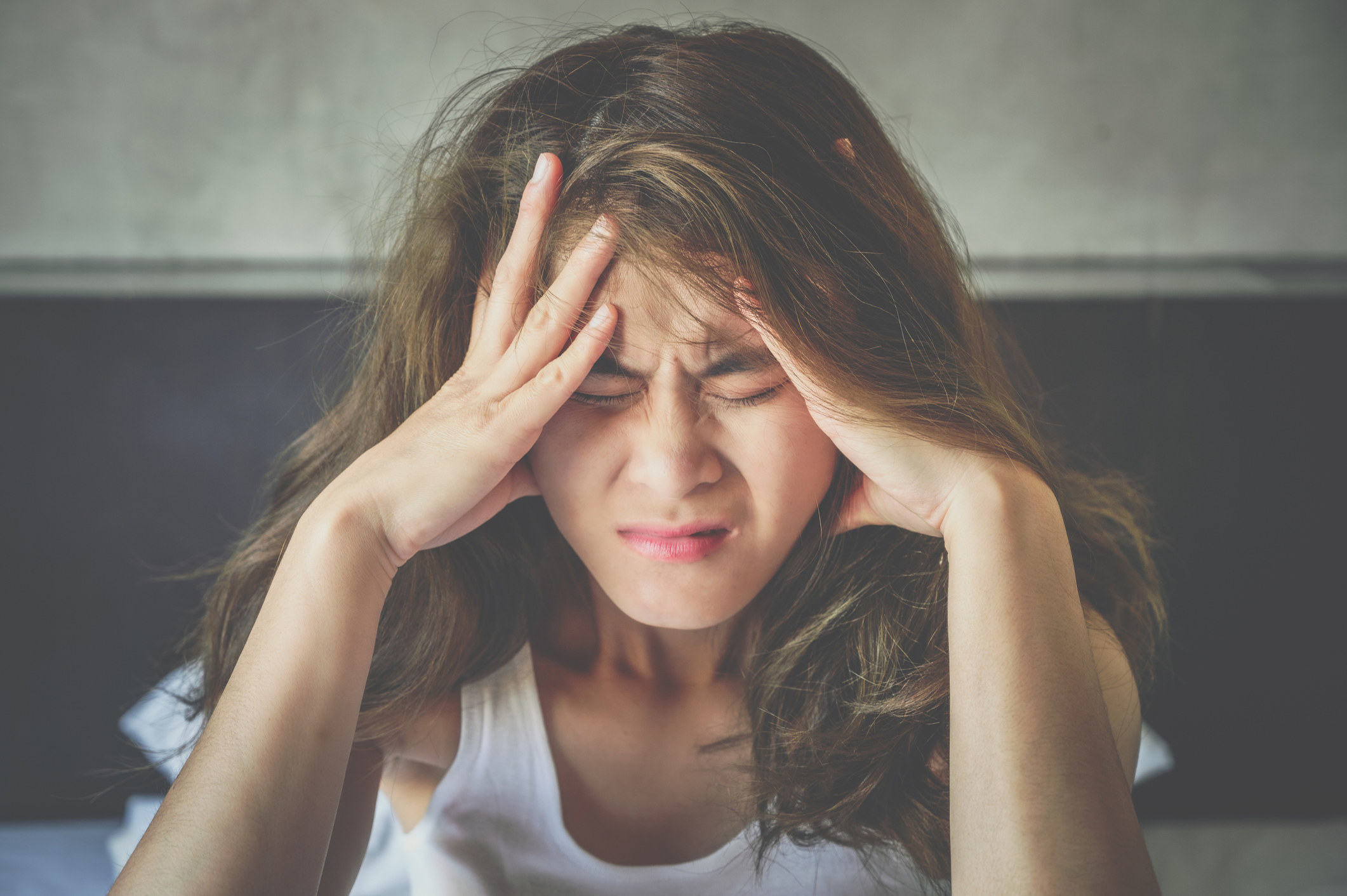 A woman with her eyes scrunched and her head in her hands