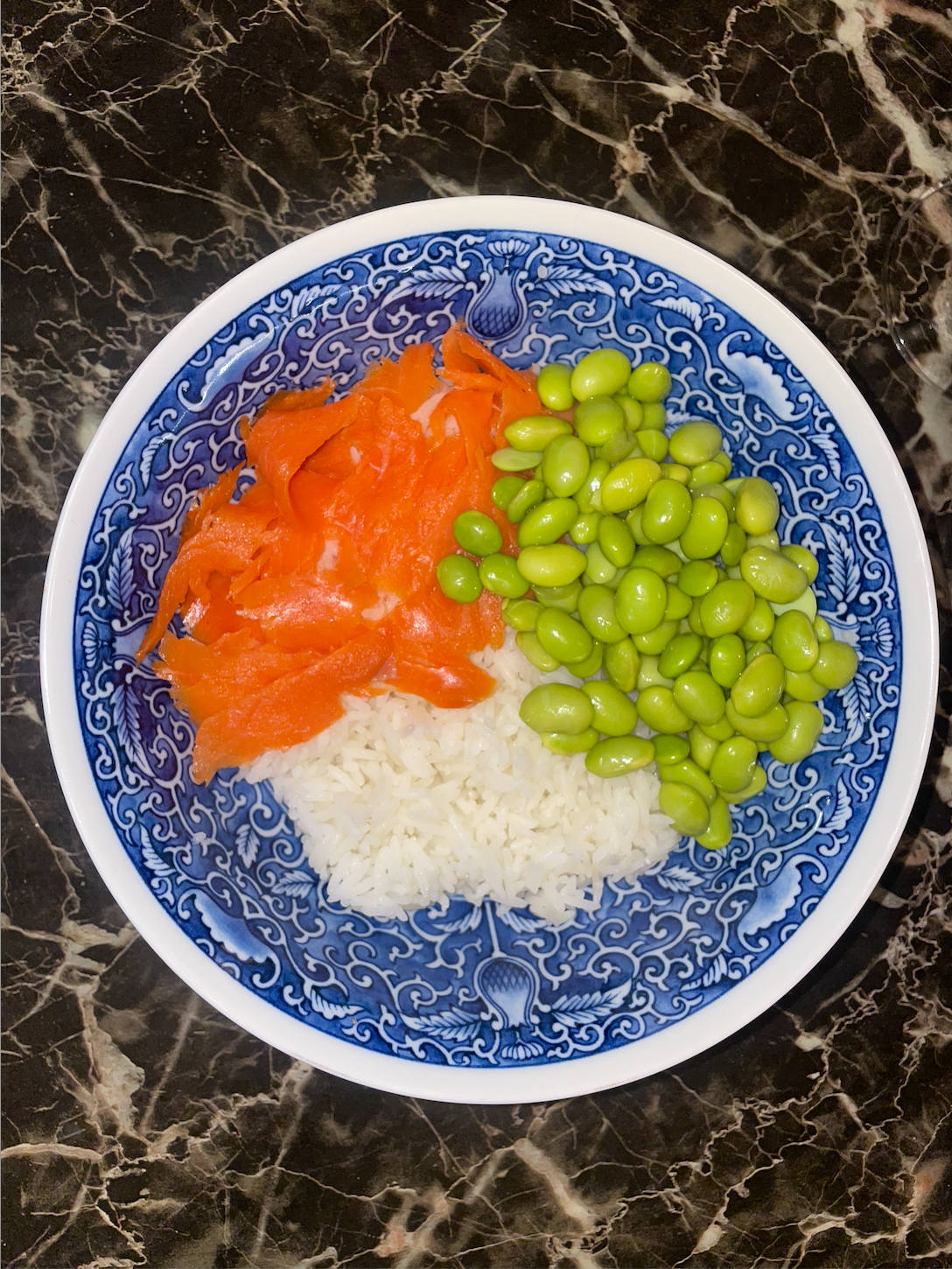A bowl containing rice, smoked salmon, and edamame