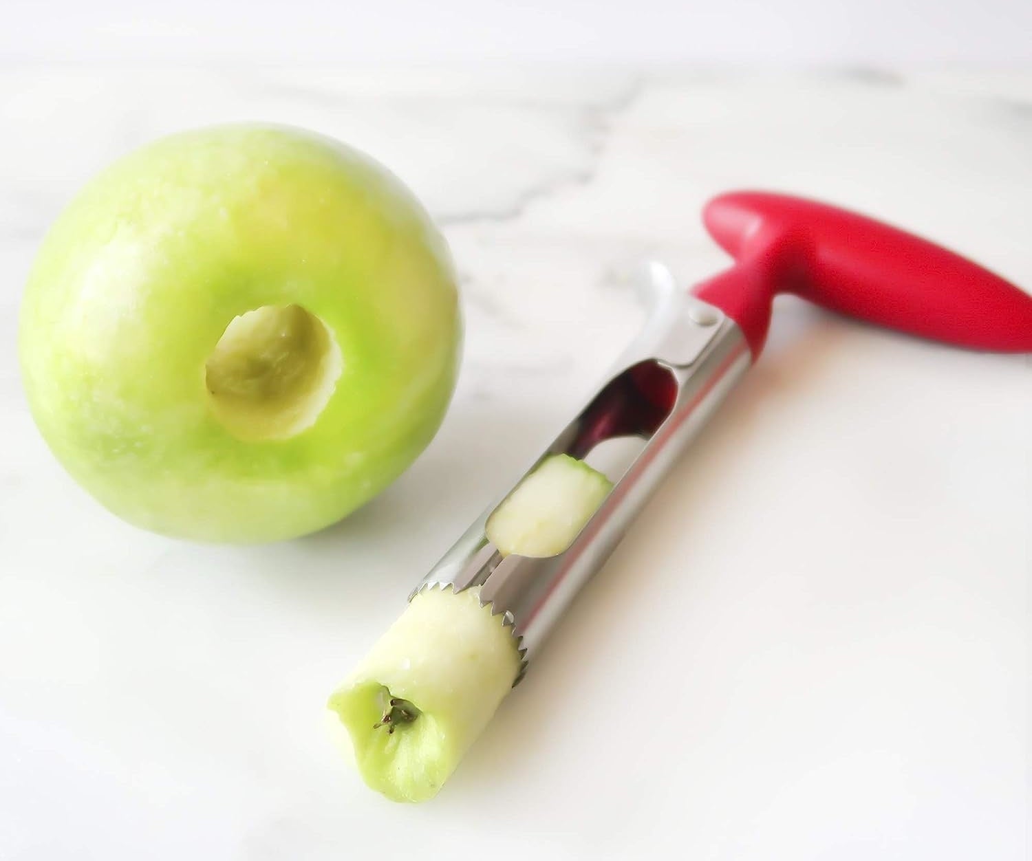Image of green apple that&#x27;s been cored by steel apple corer with red handle
