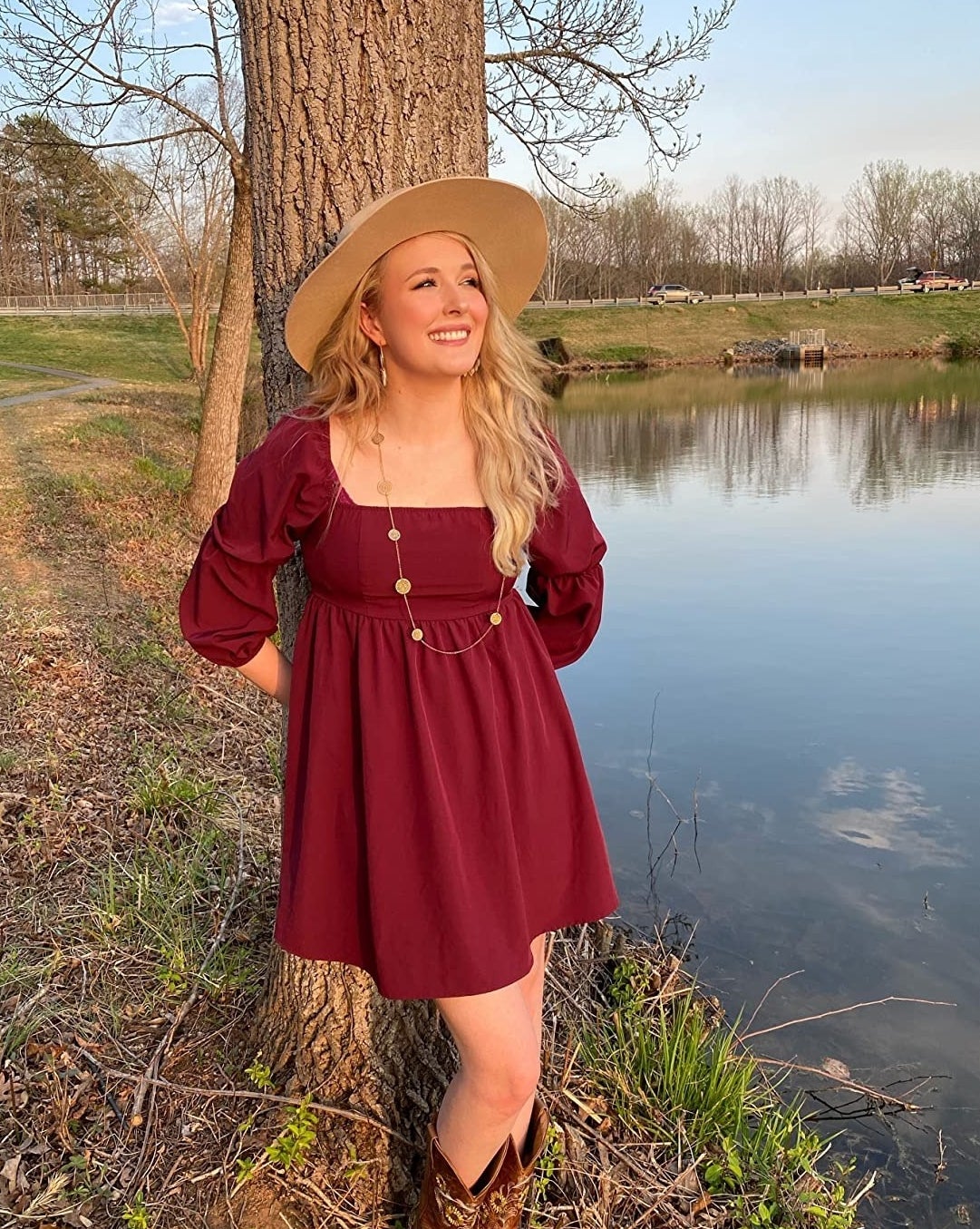 a reviewer wearing the burgundy dress next to a pond