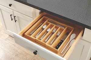 a bamboo silverware organizer holding forks, knives, spoons, a whisk, and wooden spoons