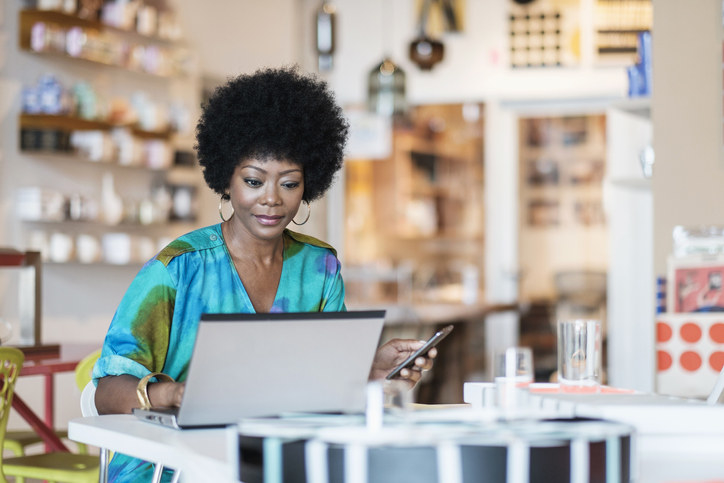 A woman using a laptop with her phone in her hand