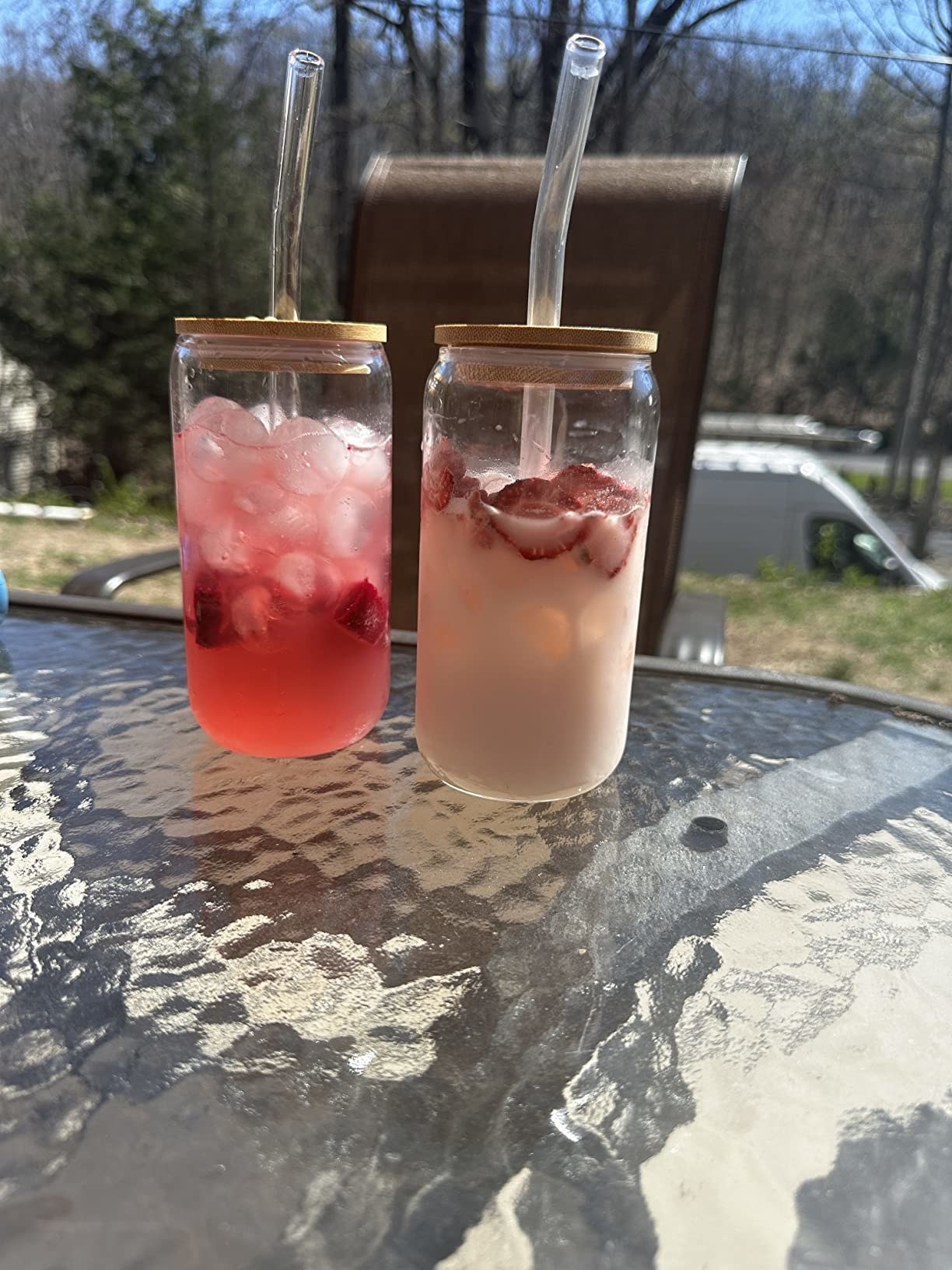 Two glasses sitting on patio table filled with cold drinks and ice and secured with wooden lid and straws