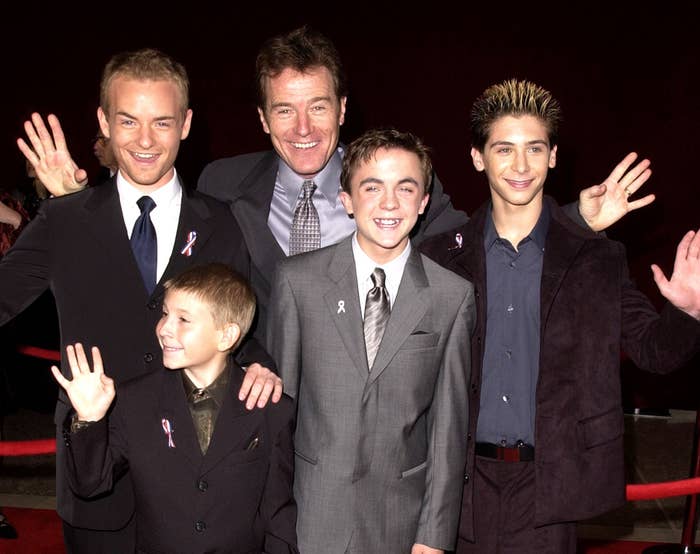 The cast waves while standing on a red carpet