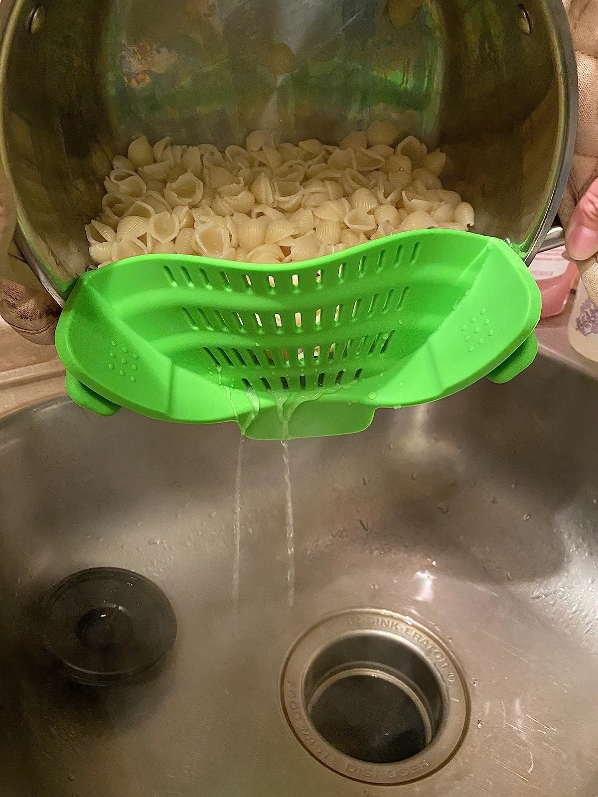 Reviewer straining water from pot of shell pasta noodles with green clip-on strainer attached to pot rim
