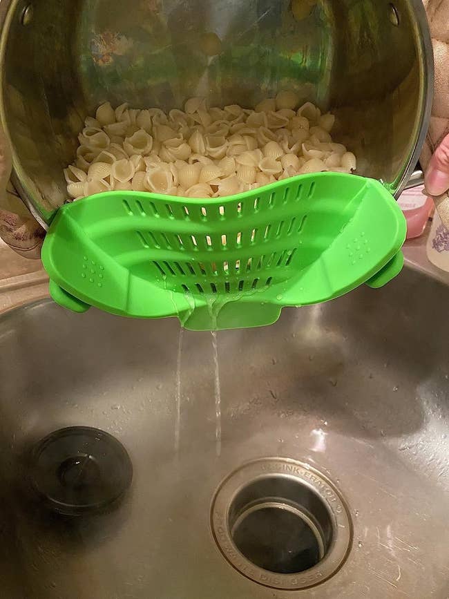 Reviewer straining water from pot of shell pasta noodles with green clip-on strainer attached to pot rim