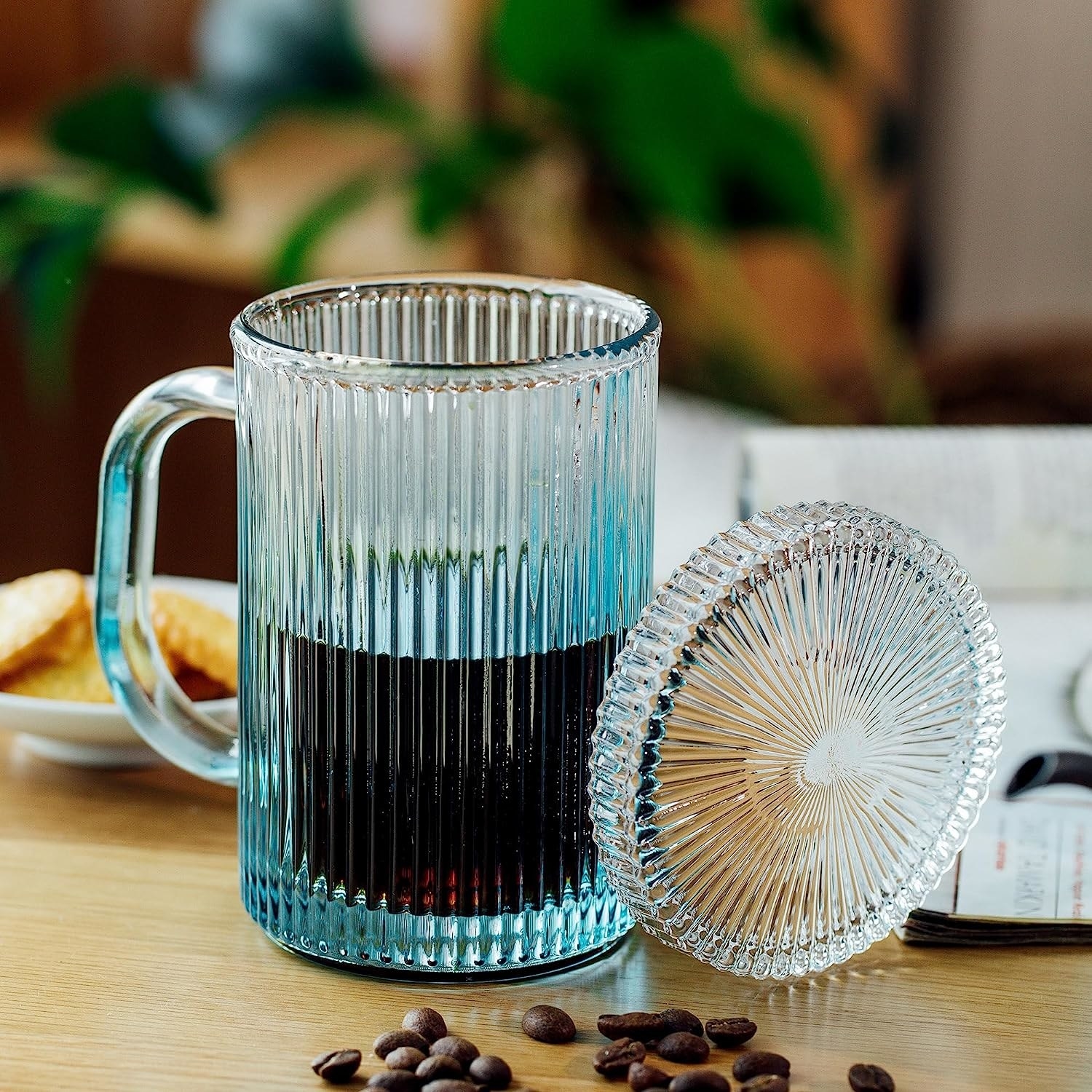 The blue mug with coffee and lid resting on side of mug