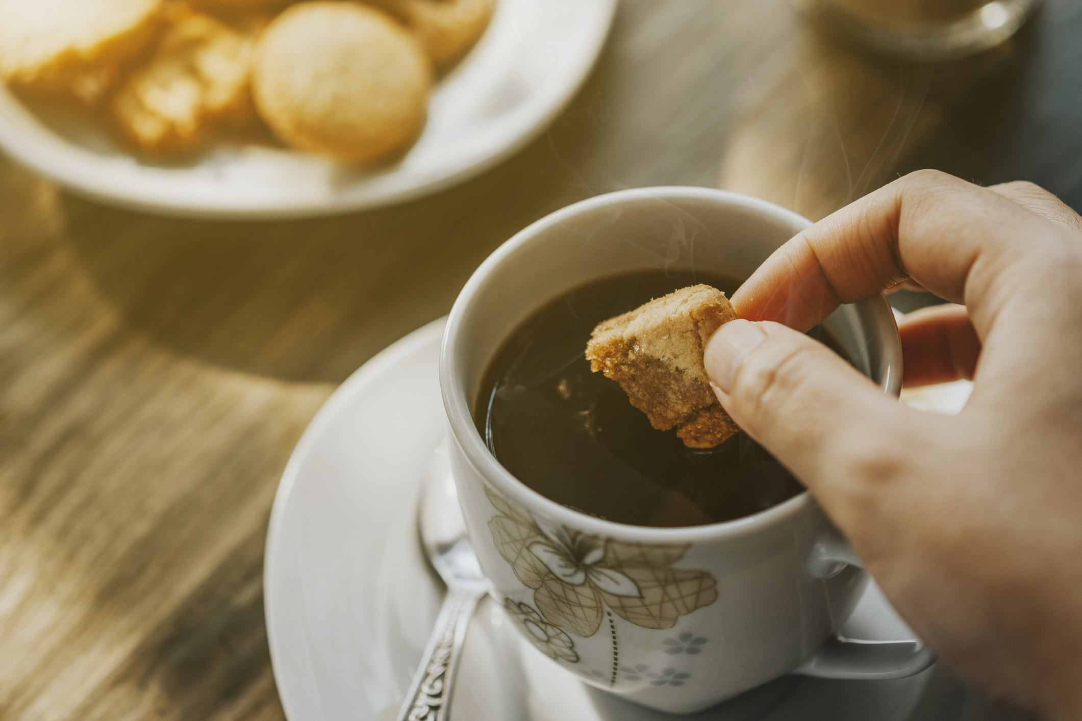 A hand dipping a cookie in coffee.