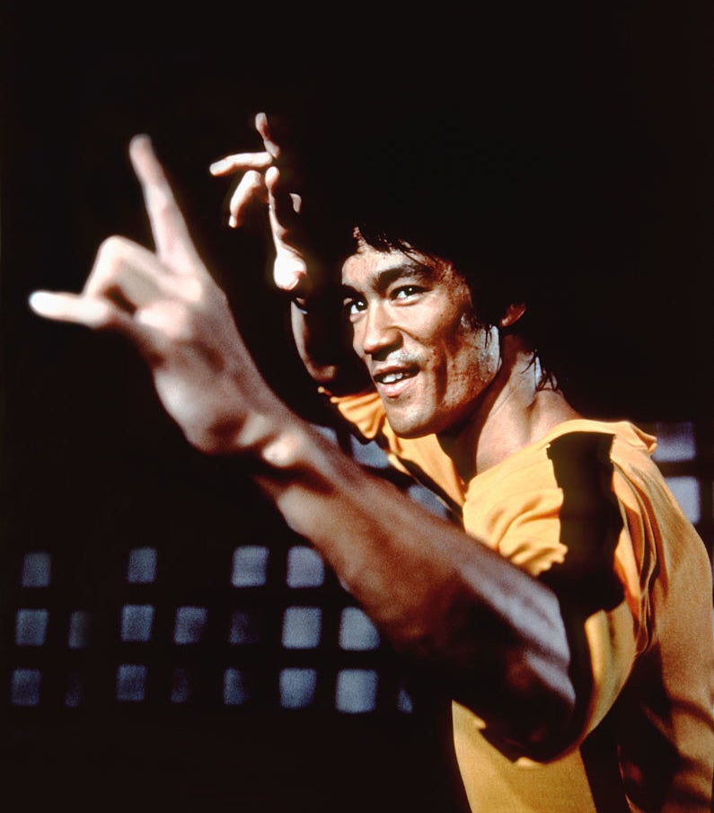 bruce lee in a fighting stance wearing his iconic yellow with black stripe outfit from game of death