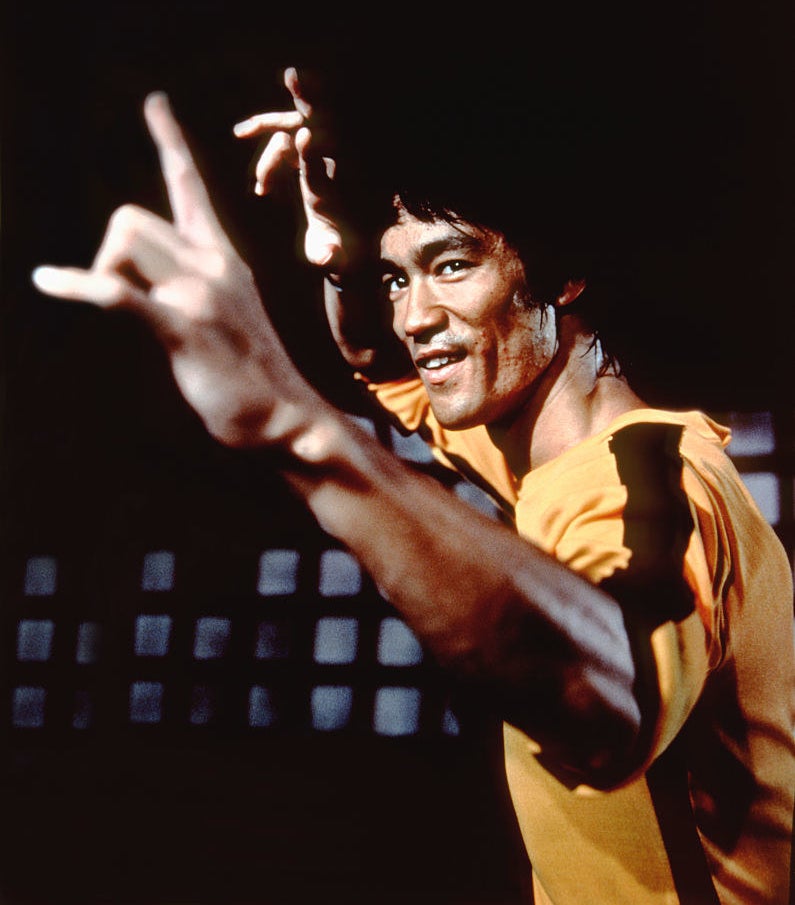 bruce lee in a fighting stance wearing his iconic yellow with black stripe outfit from game of death