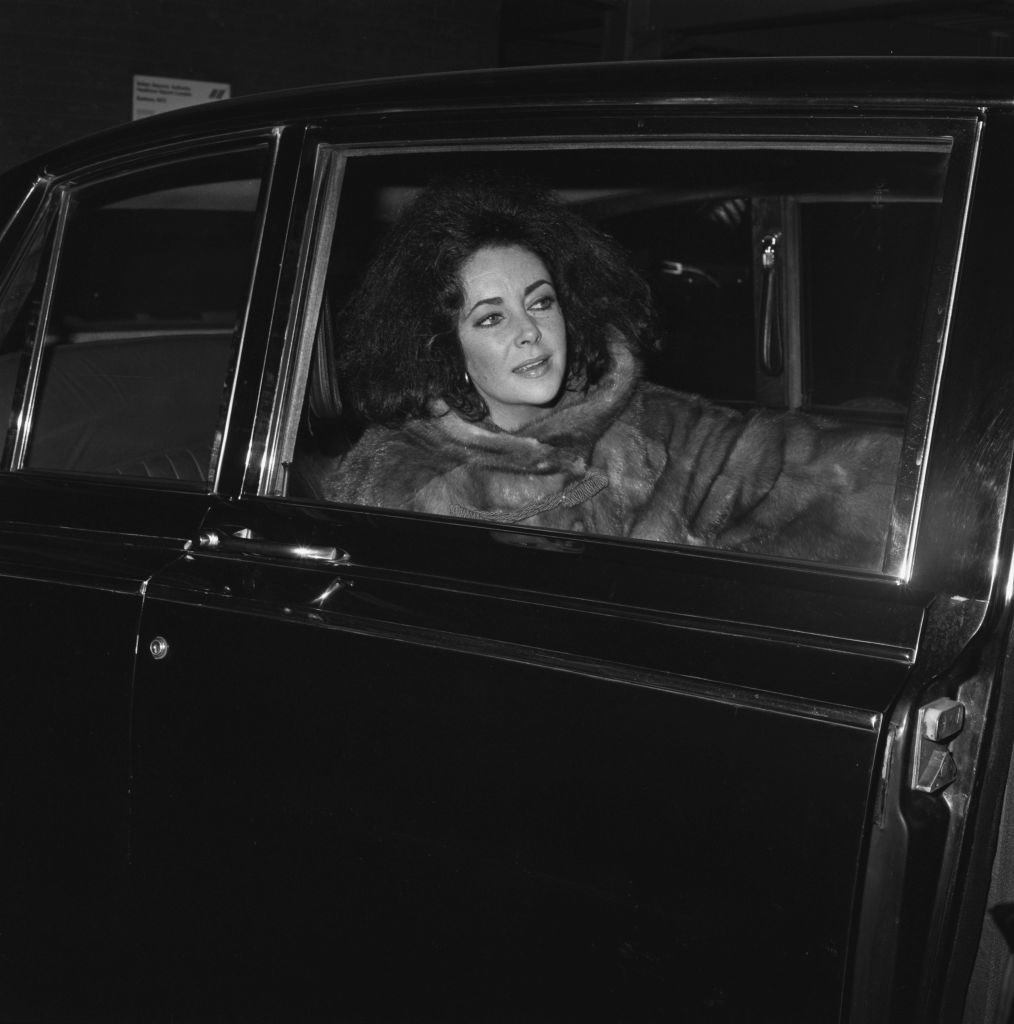 Elizabeth Taylor in a fur coat sitting in the back of a car