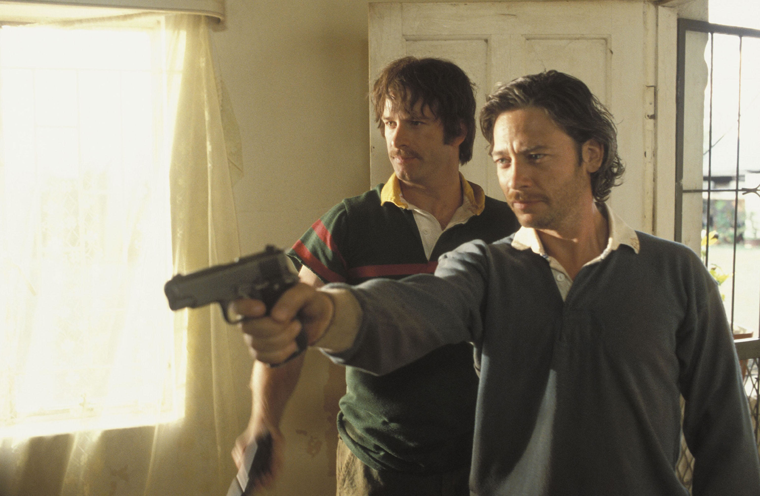 Two gruff men hold guns in a bare apartment