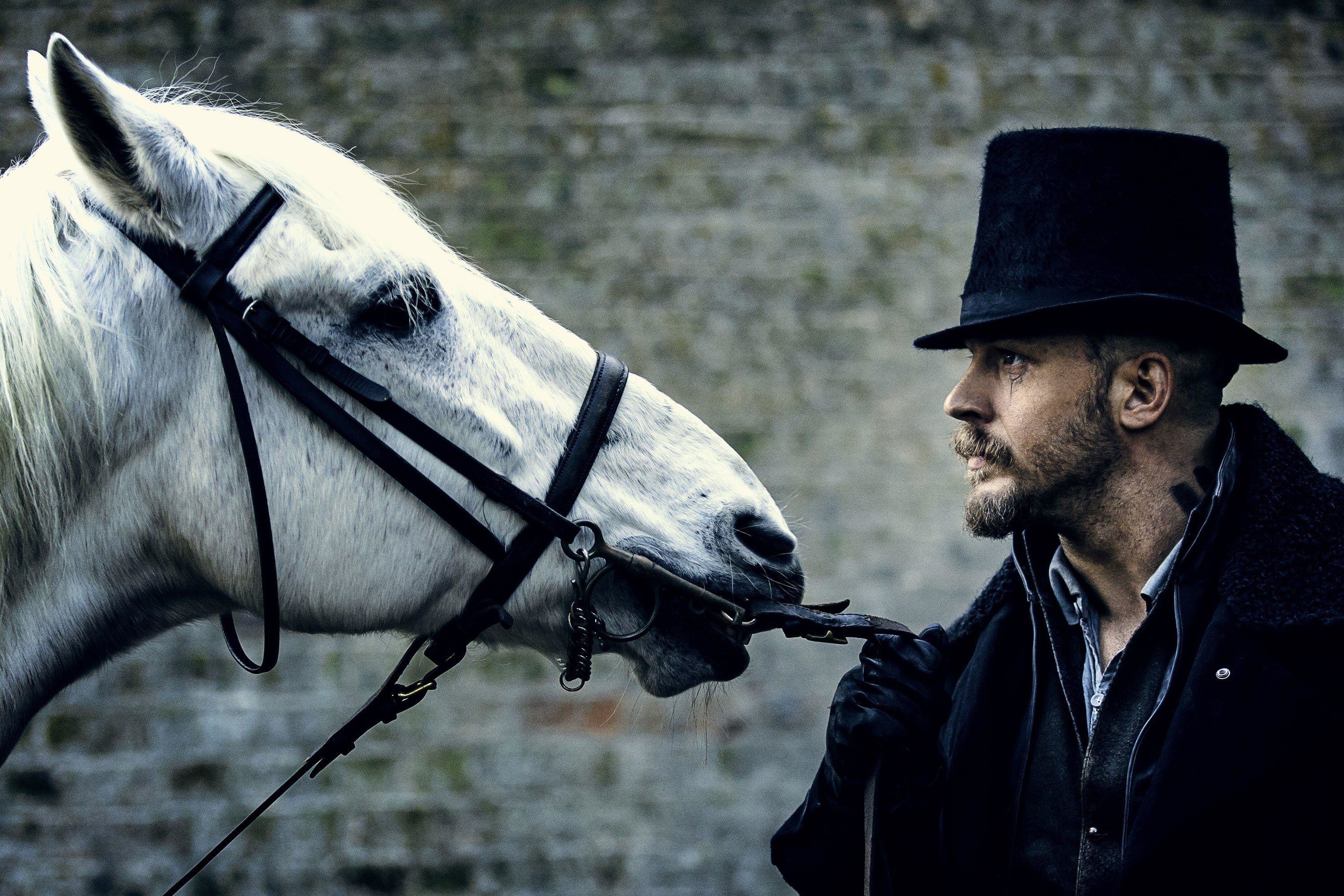 Tom Hardy in a top hat stares at a white horse