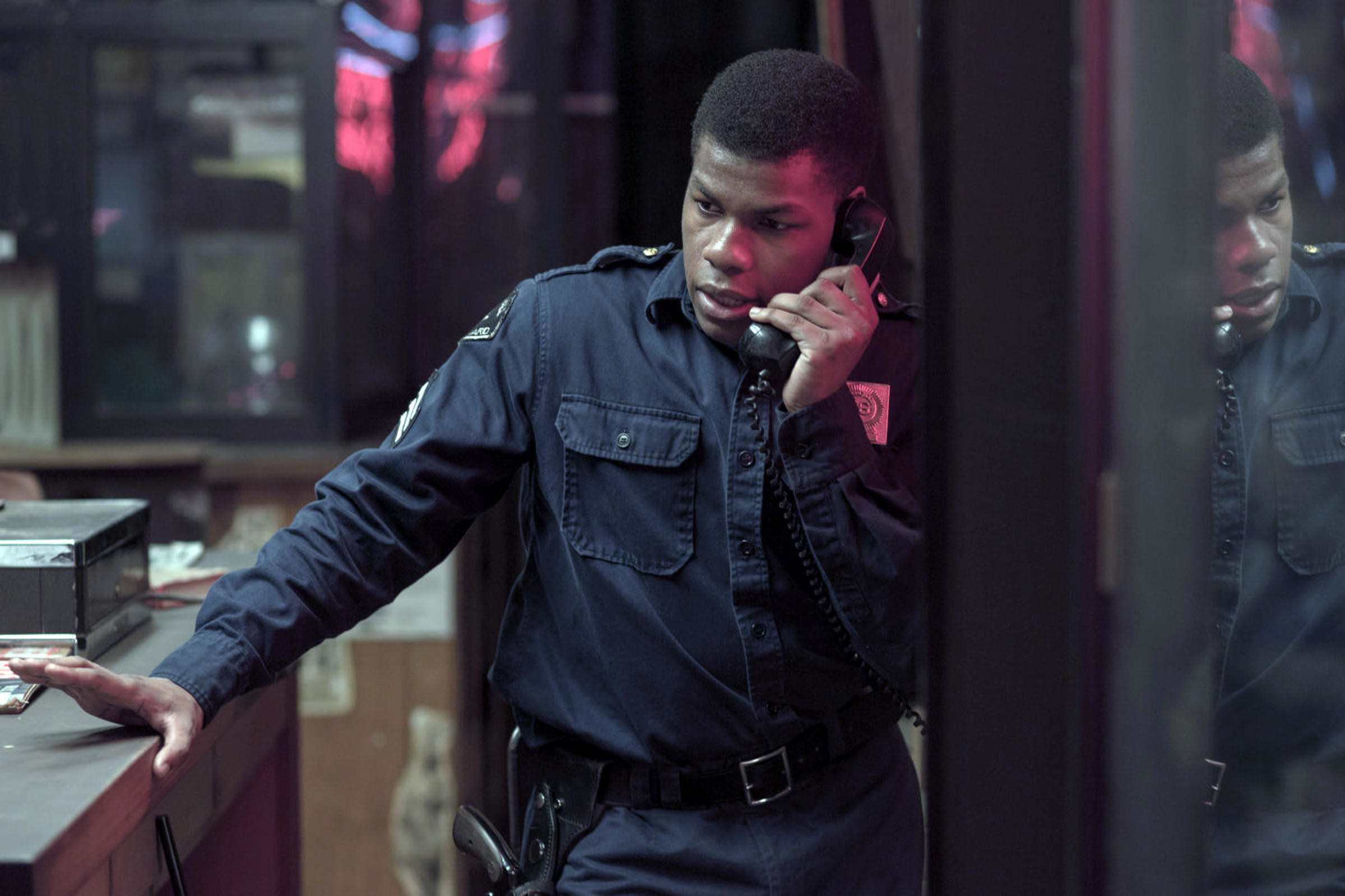 John Boyega in a cop costume listens during a tense phone conversation