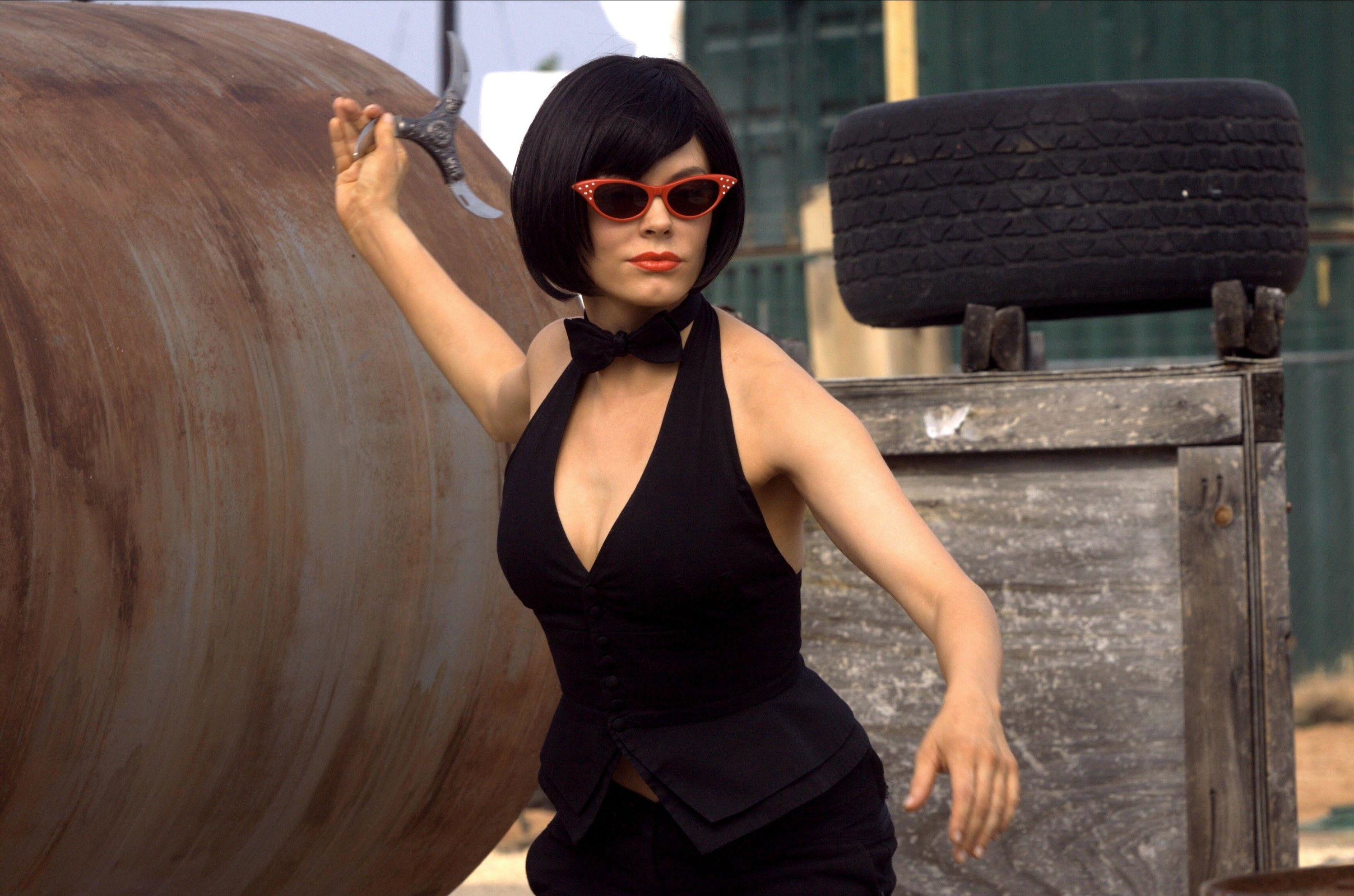 Rose McGowan holds a three-sided blade in a black dress and sunglasses