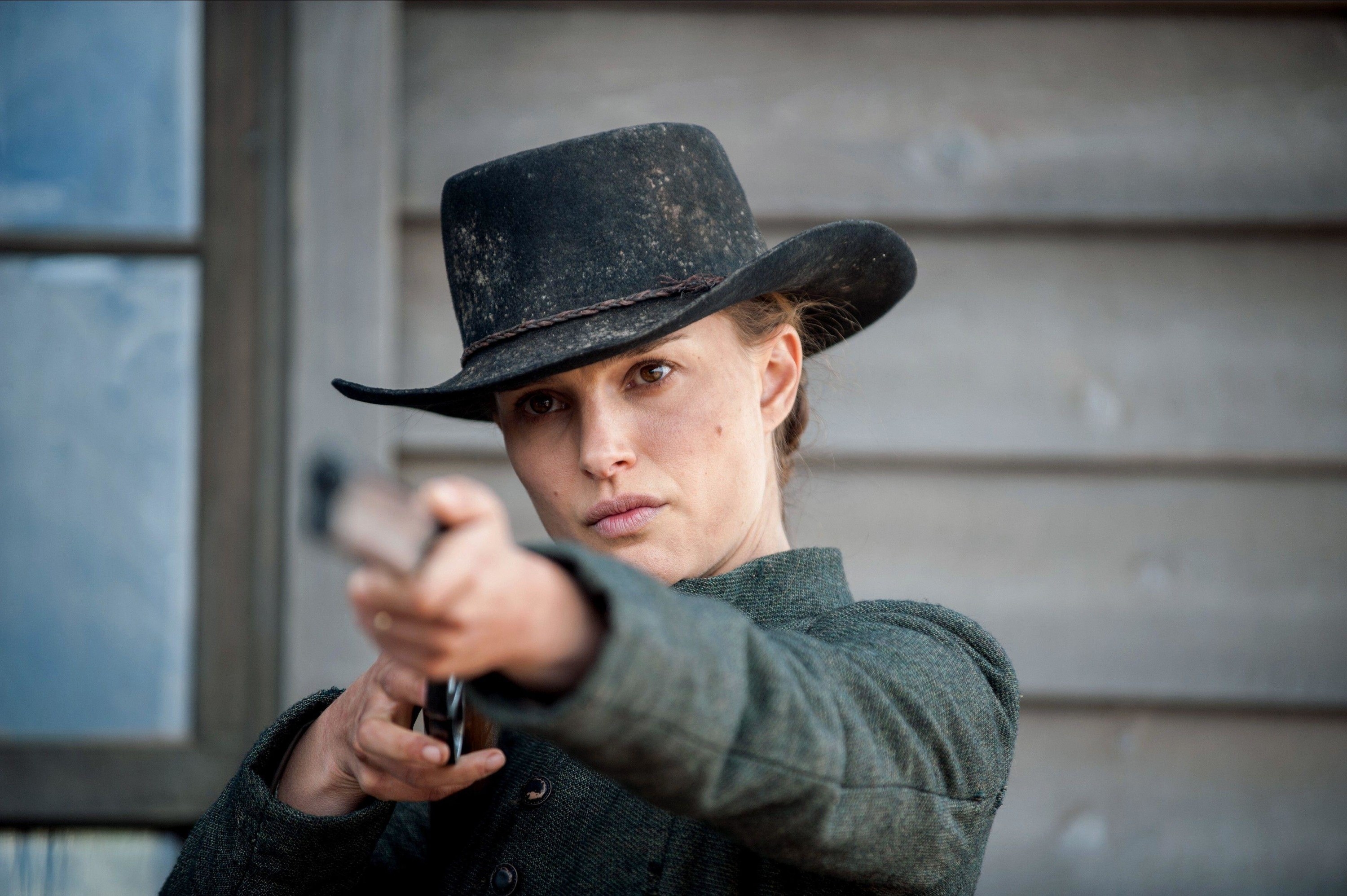 Natalie Portman points a rifle in a dusty western get-up