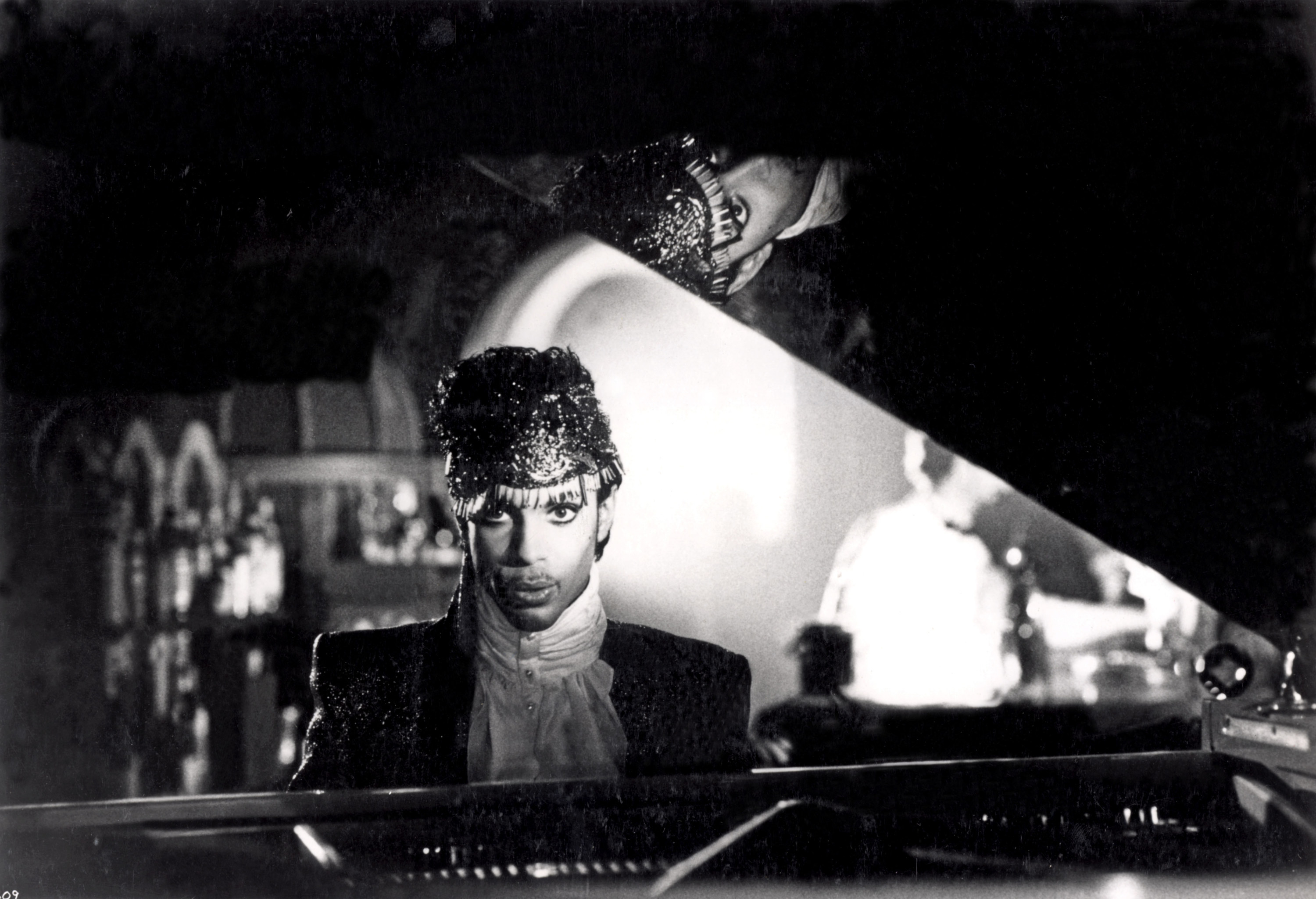 Prince sits behind a piano in black-and-white
