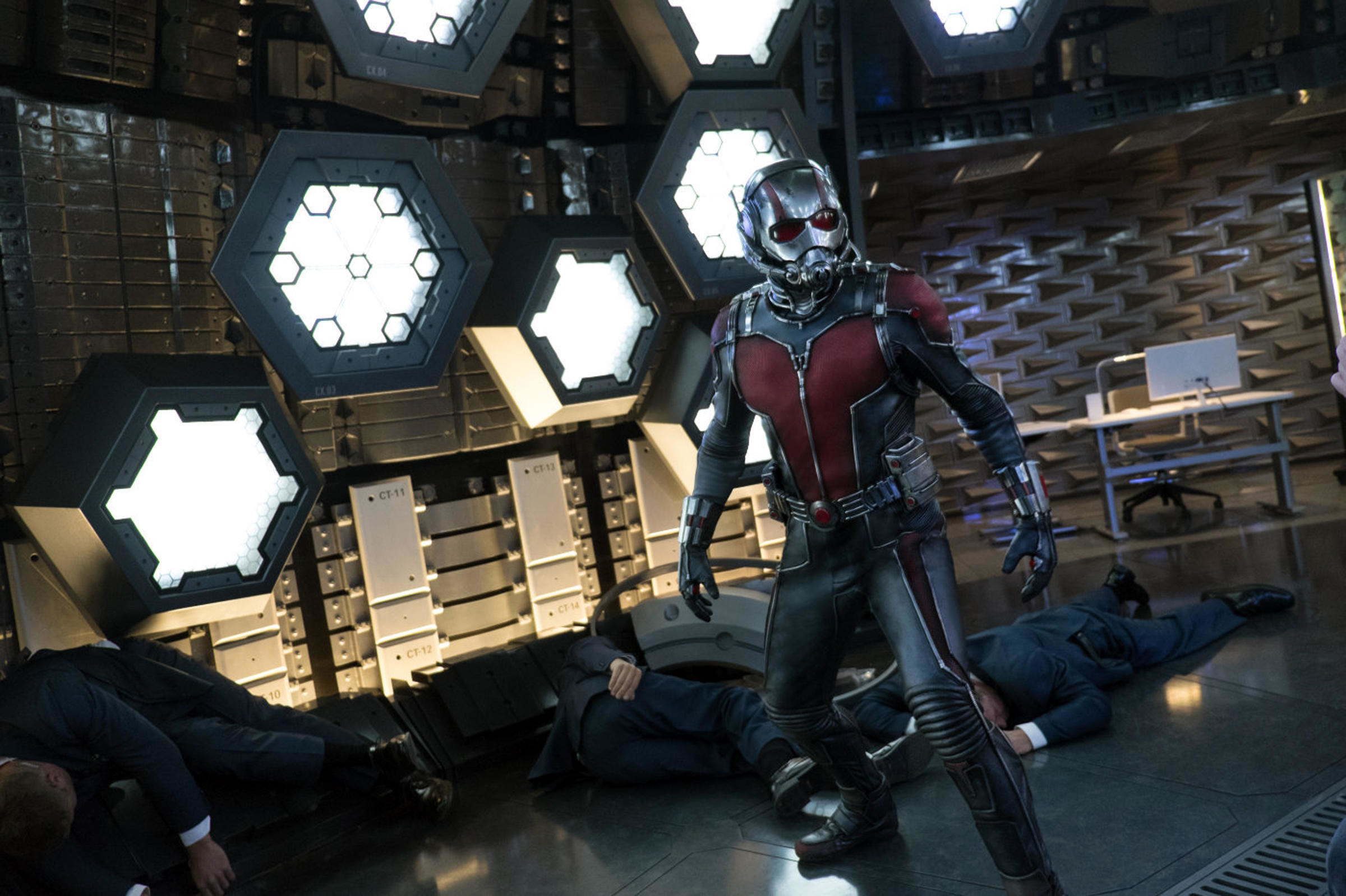 Ant-Man poses in a futuristic laboratory filled with unconscious guards
