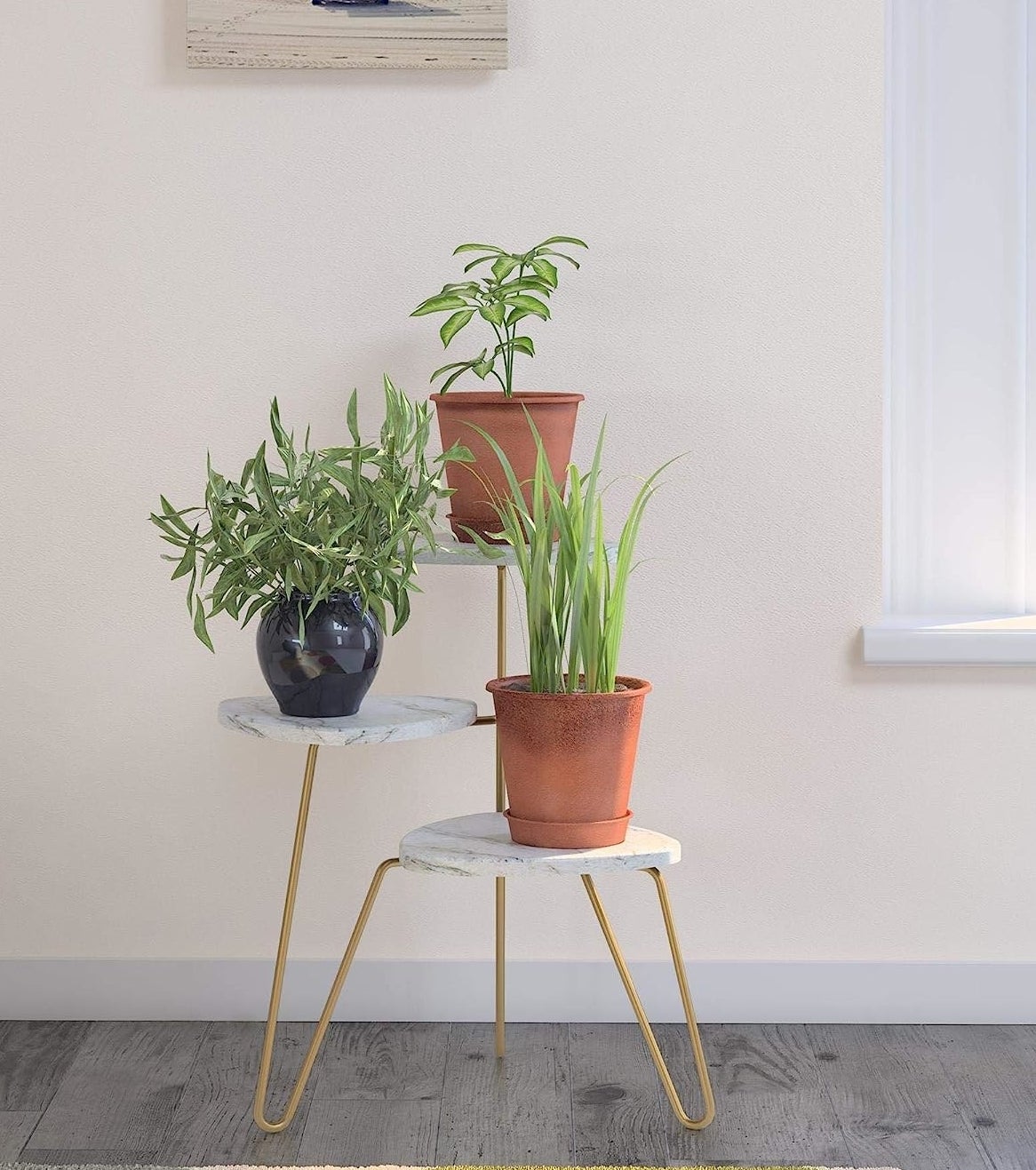 The white marble and gold metal plant stand displays three plants