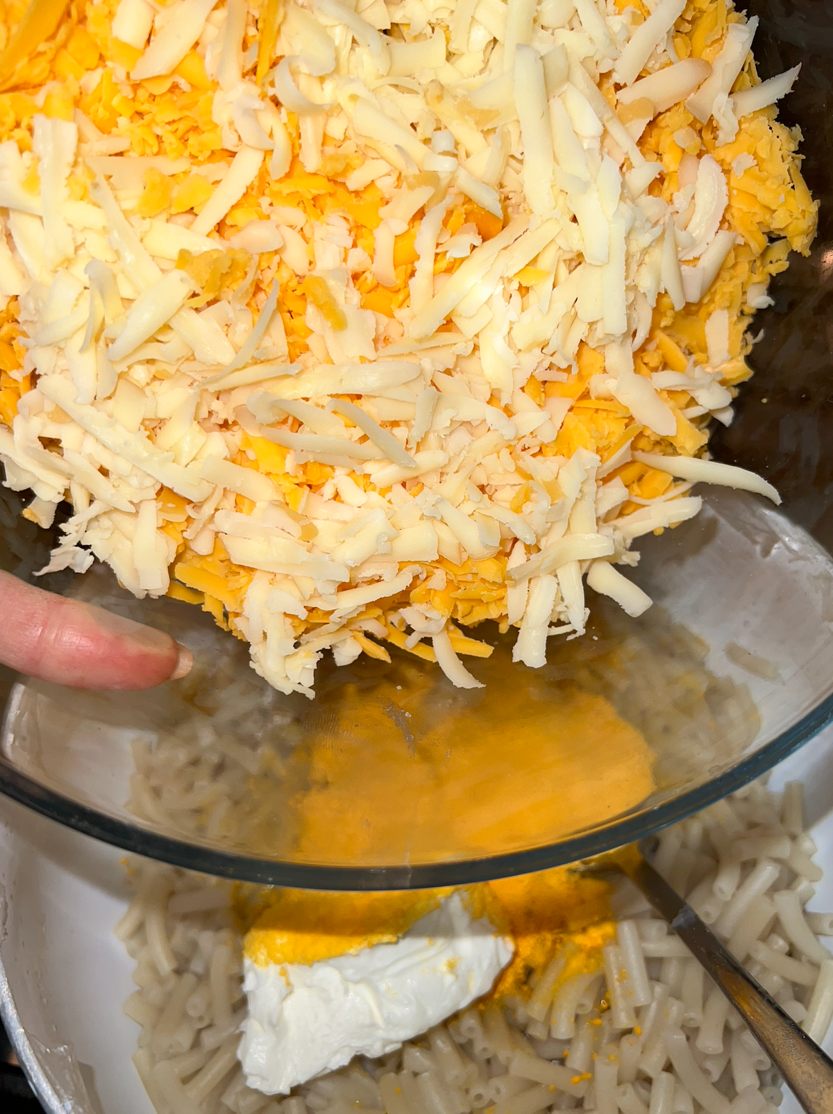 Grated cheeses being added to mac, cheese powder, and cream cheese