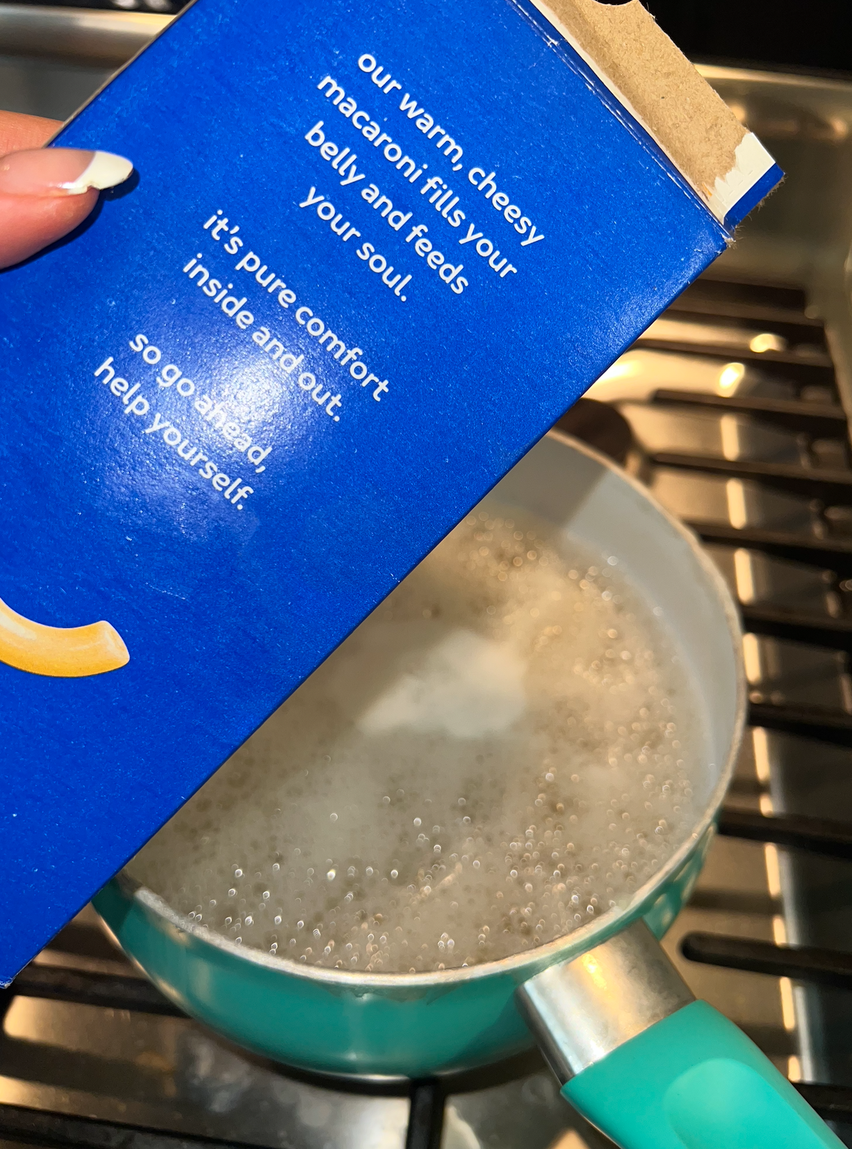 A box of mac held over a pan of boiling water