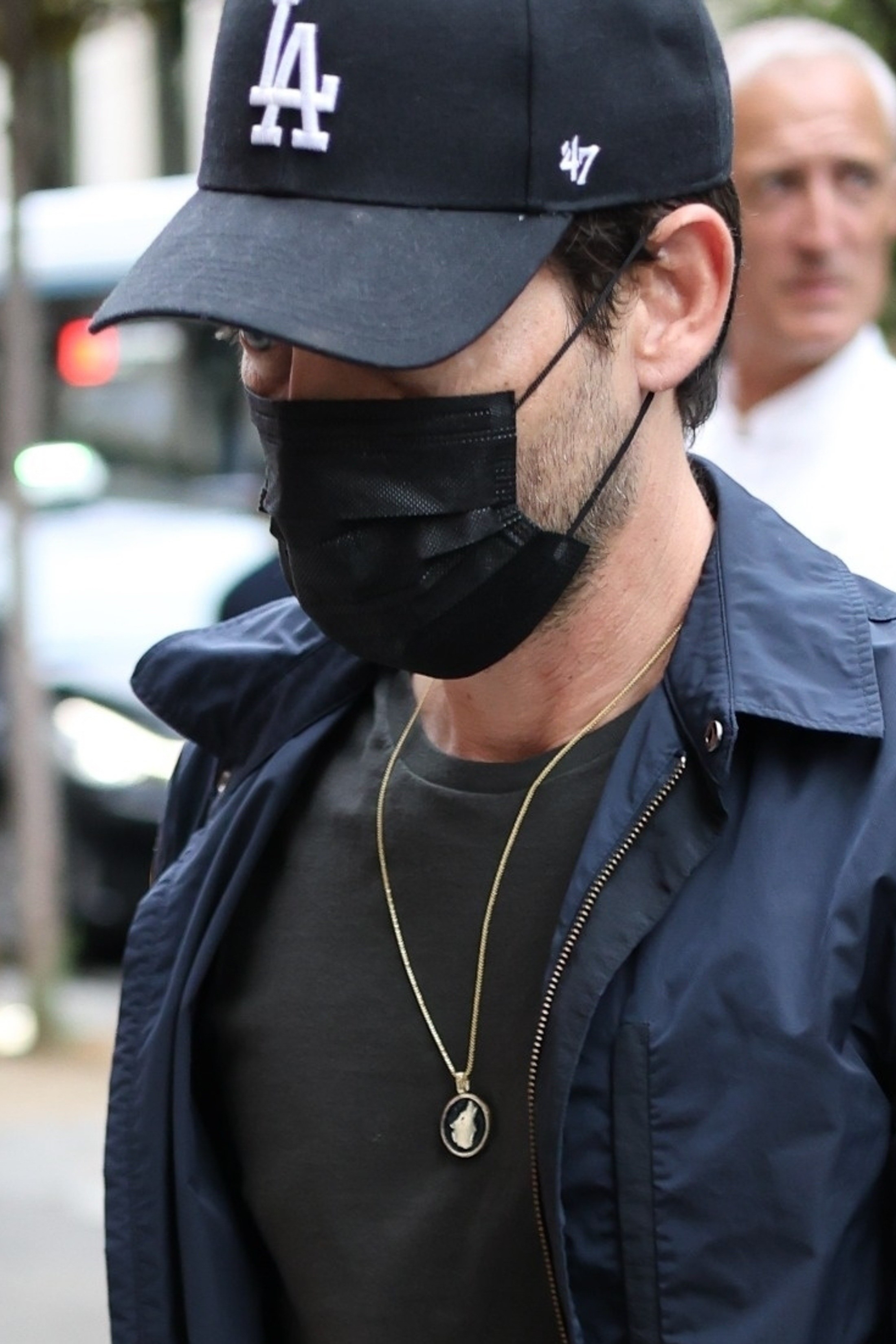 Close-up of Tobey wearing a cap, necklace, and surgical mask