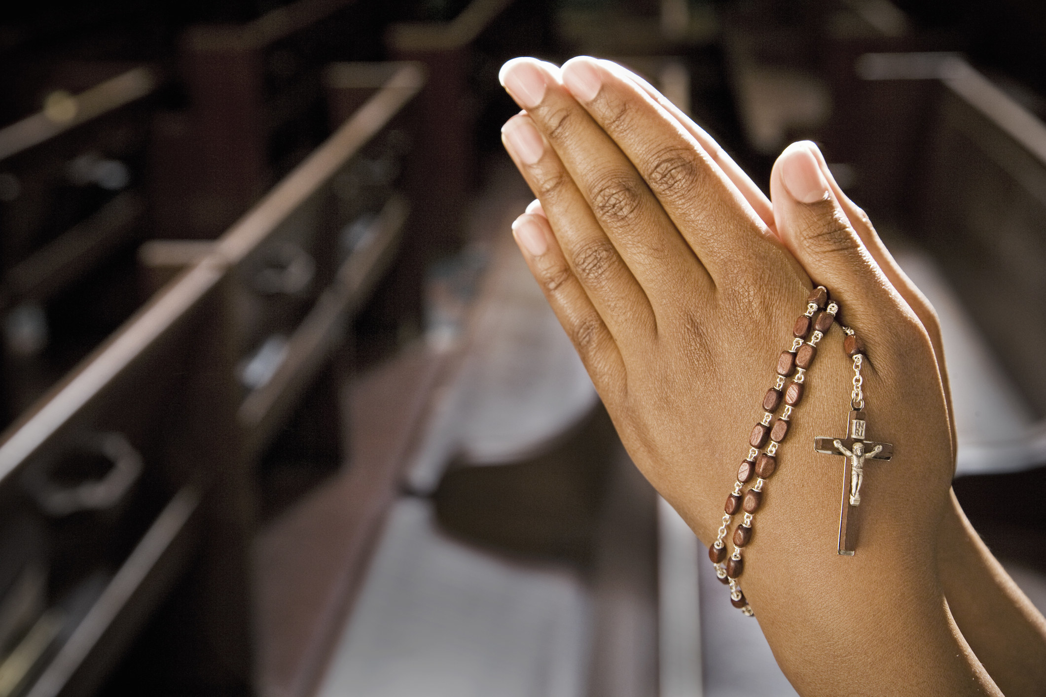 Woman folding her hands in church with rosary beads