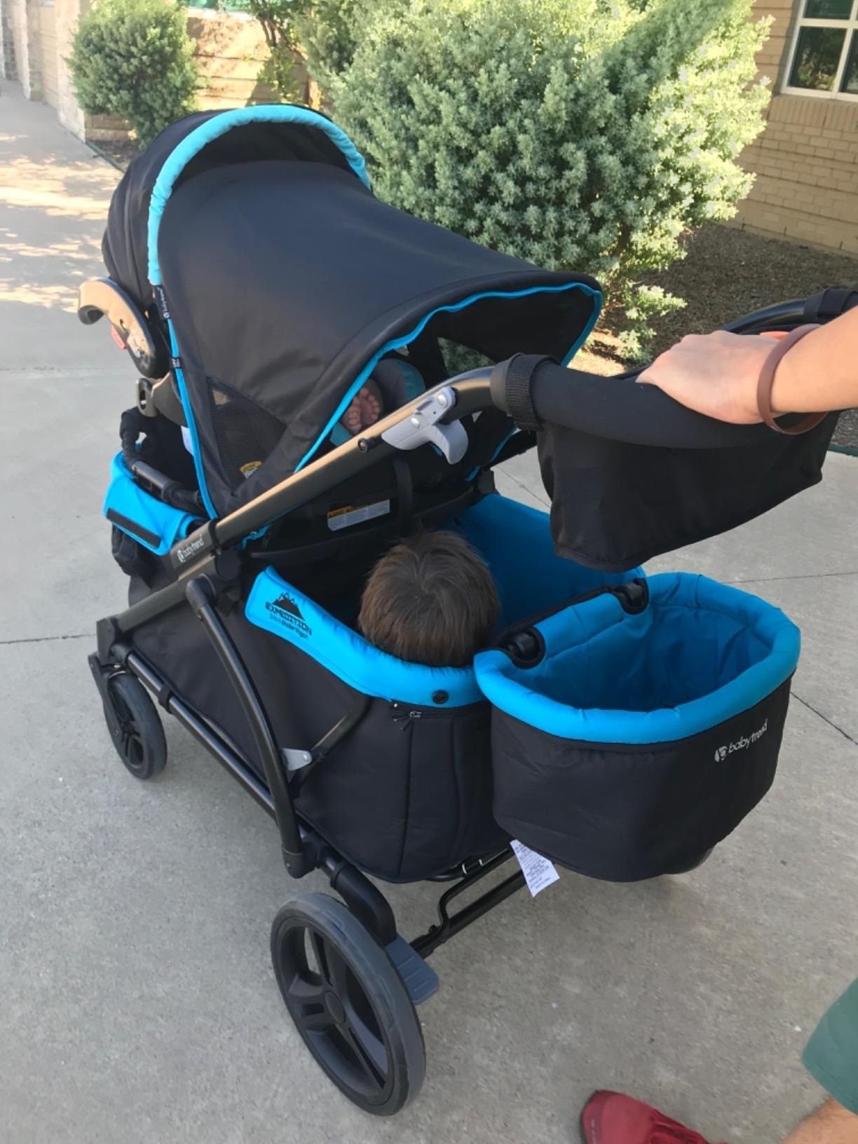 Person pushes a wagon with a baby carrier and a child in it