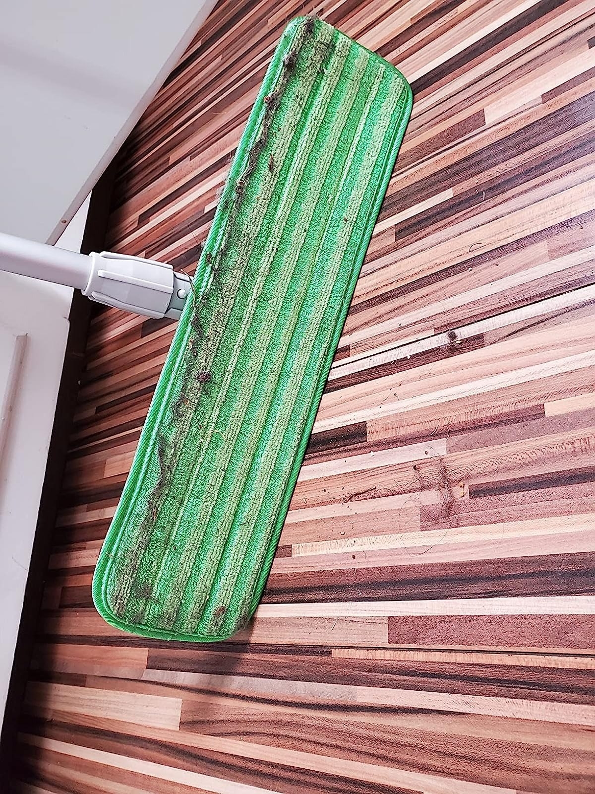 green mop with pet hairs above hardwood floor