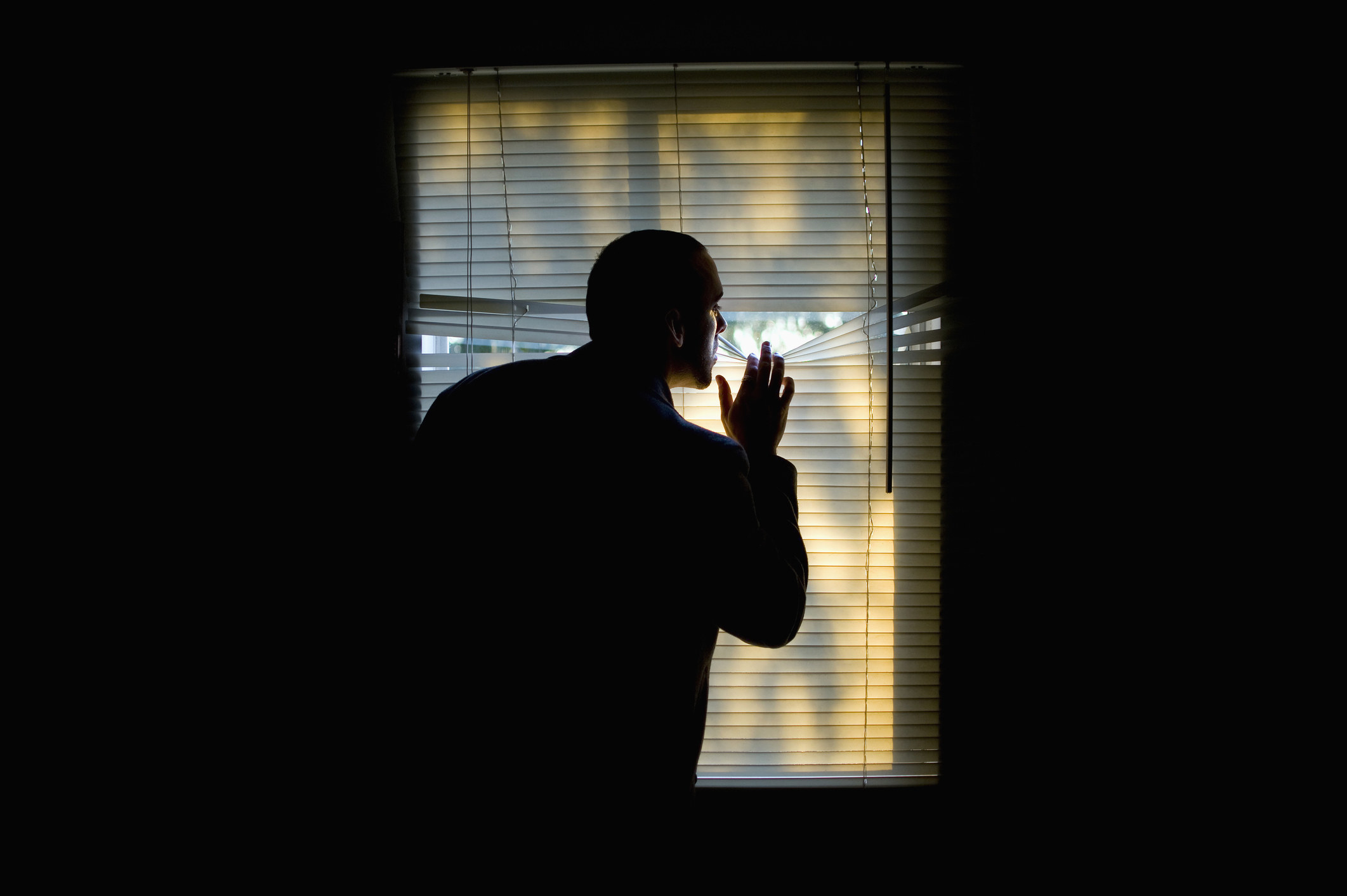 a man is in a dark room peeking through the blinds