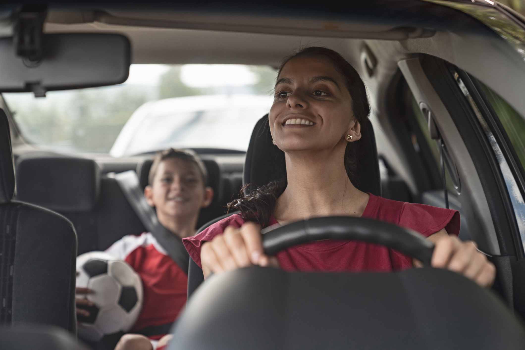 A mother looking at her son in the backseat of a car, as he holds a soccer ball