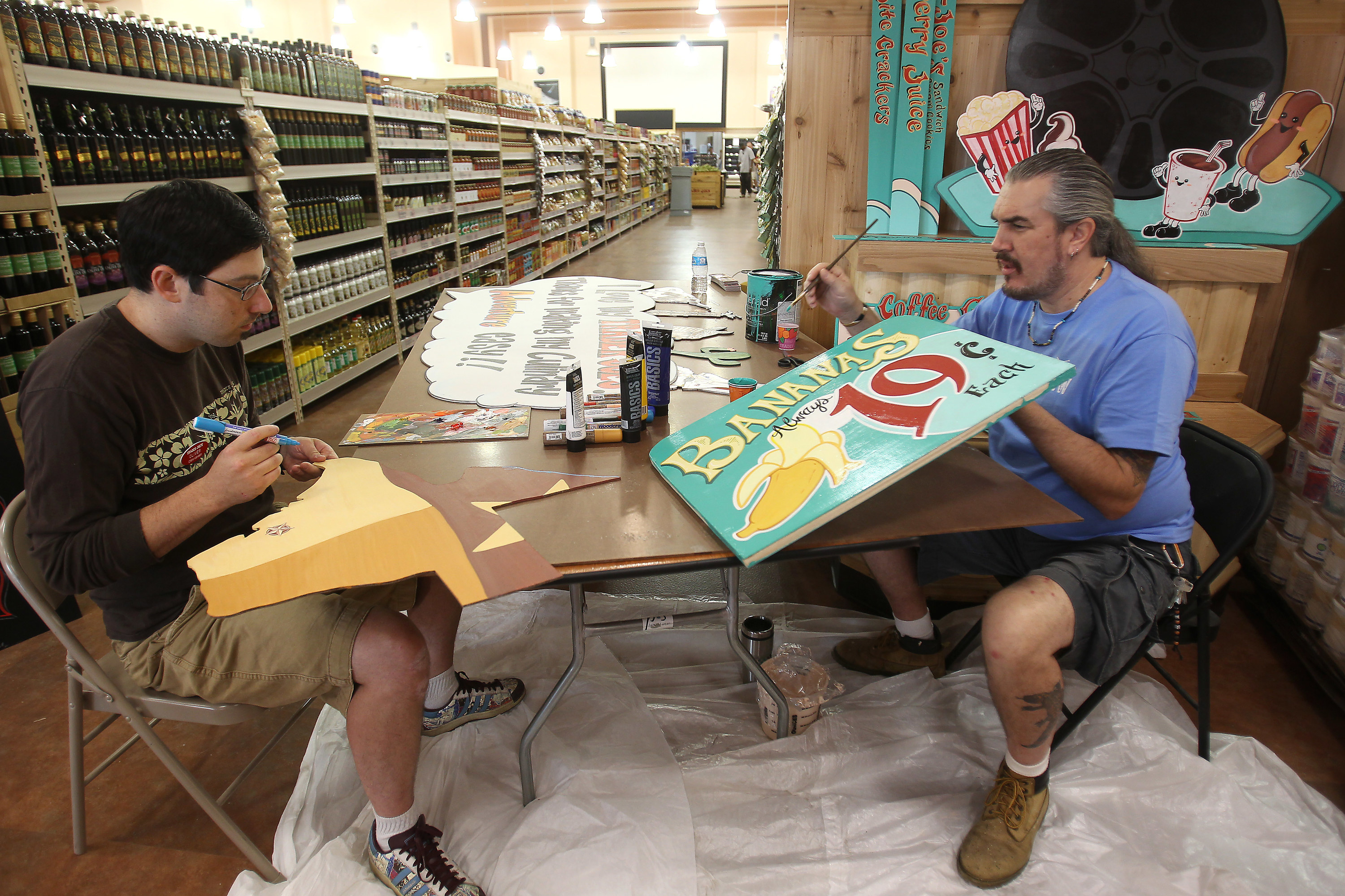 Two Trader Joe&#x27;s employees hand-painting signs for the store