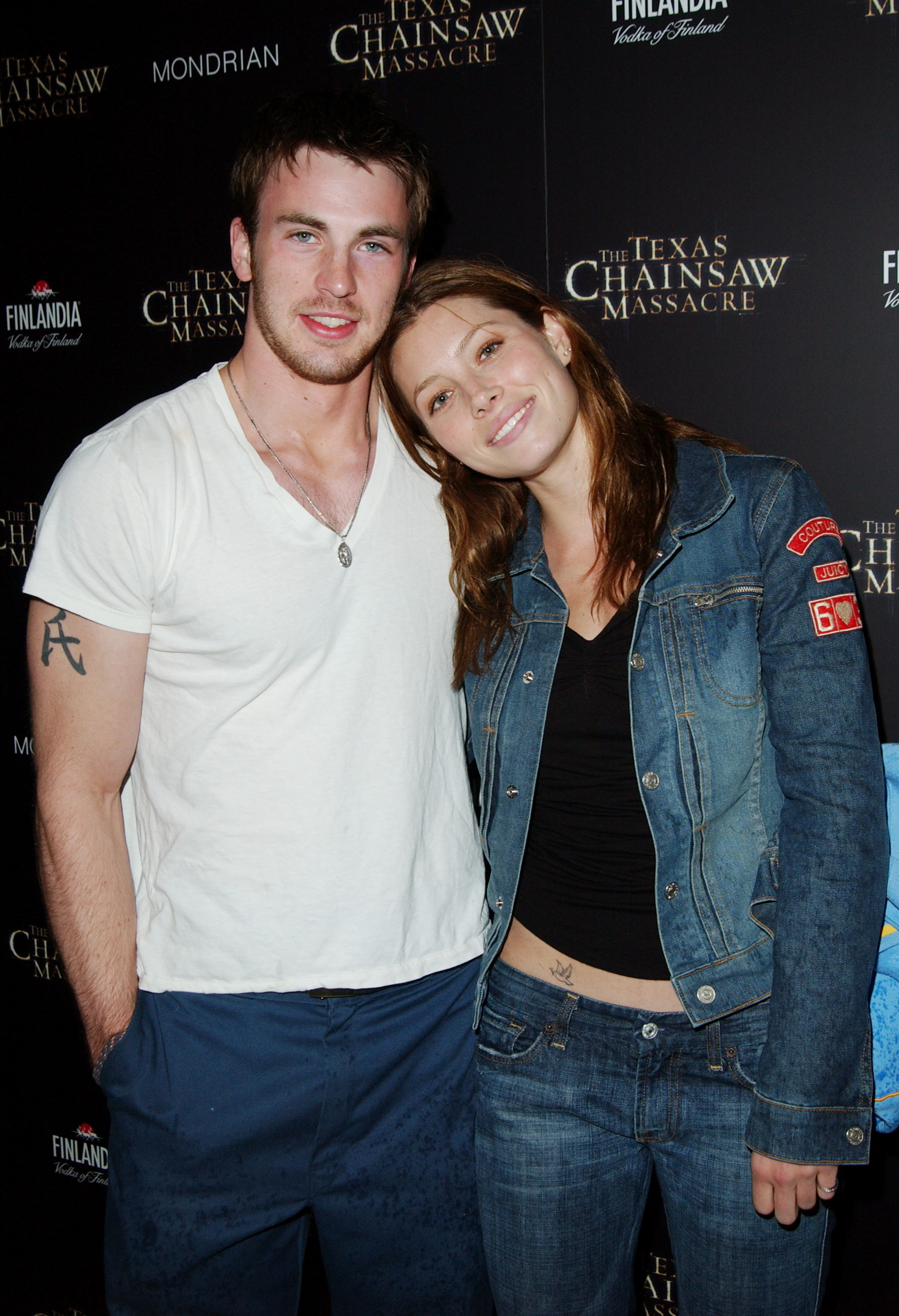 Chris Evans in a tee and pants next to Jessica Biel who&#x27;s wearing a denim outfit and leaning her head against Chris&#x27;s shoulder