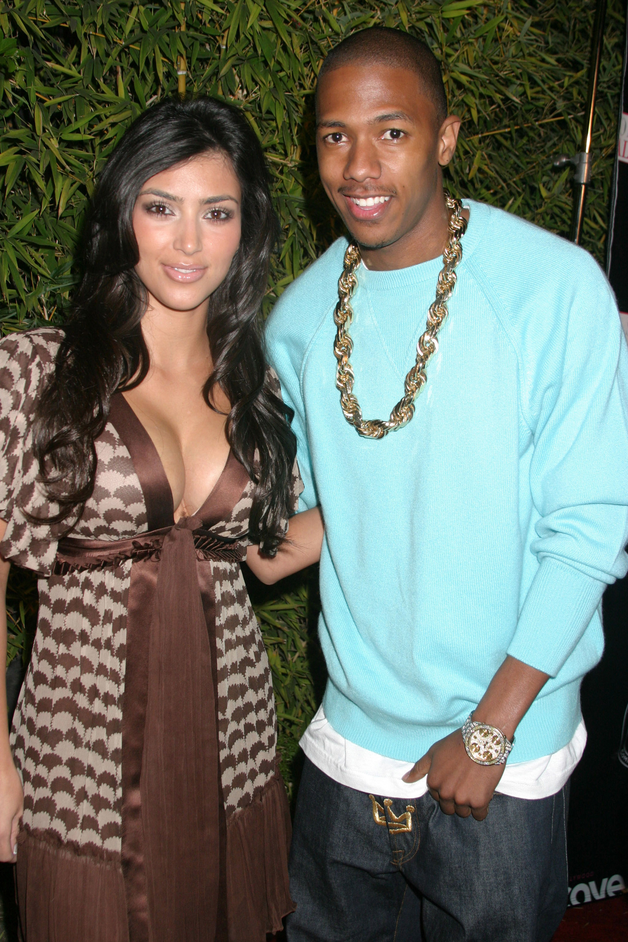 Kim Kardashian in a wrap dress standing next to Nick Cannon in a sweater and pants as they smile for the camera
