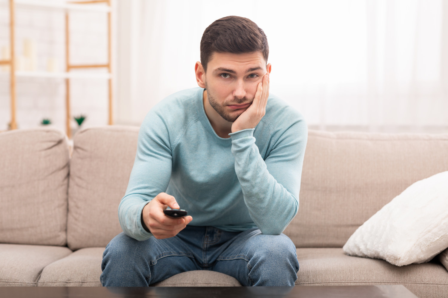 A man looking bored and holding a television remote