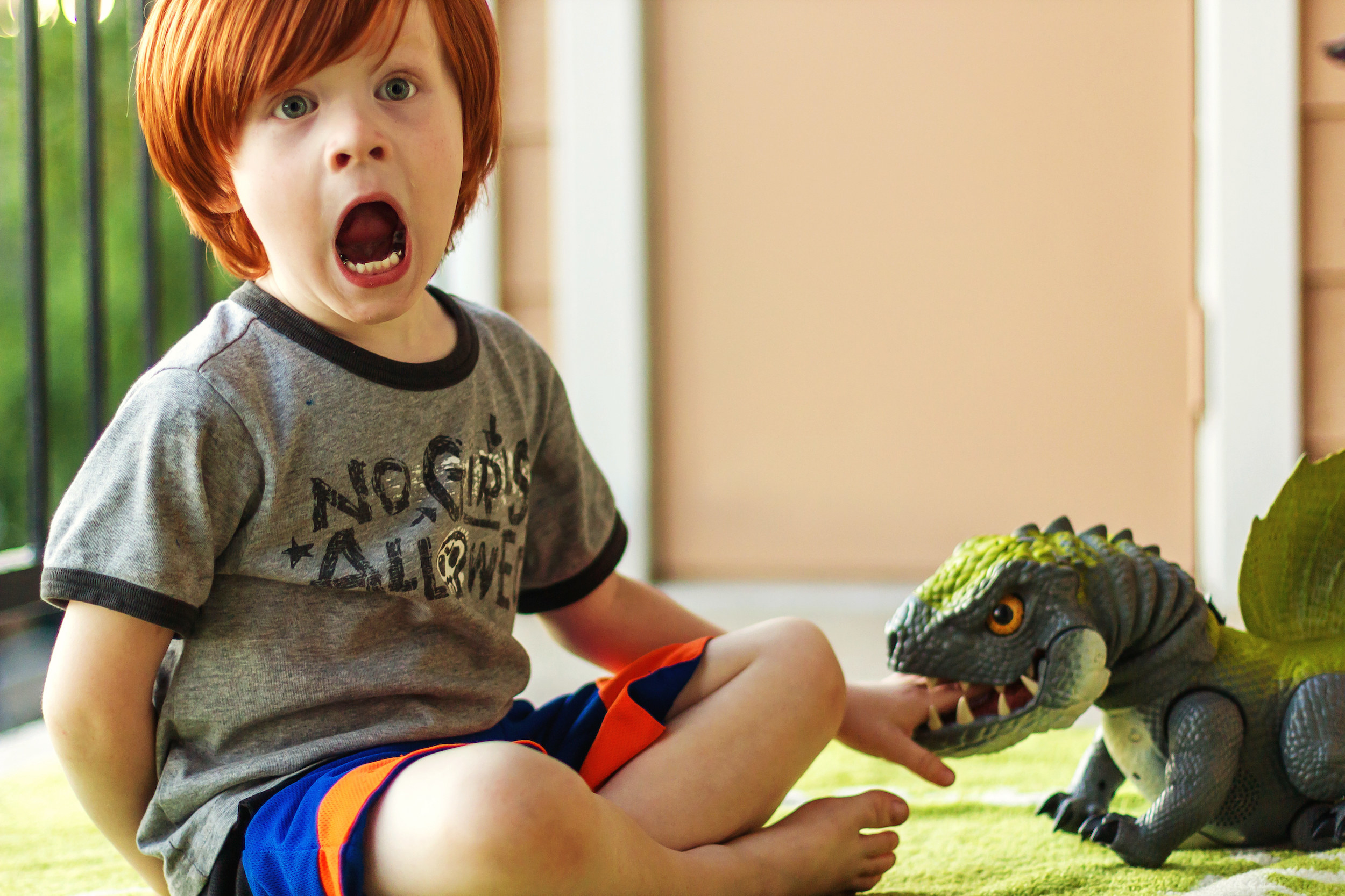 A little kid screaming with his hand in a dinosaur toy's mouth