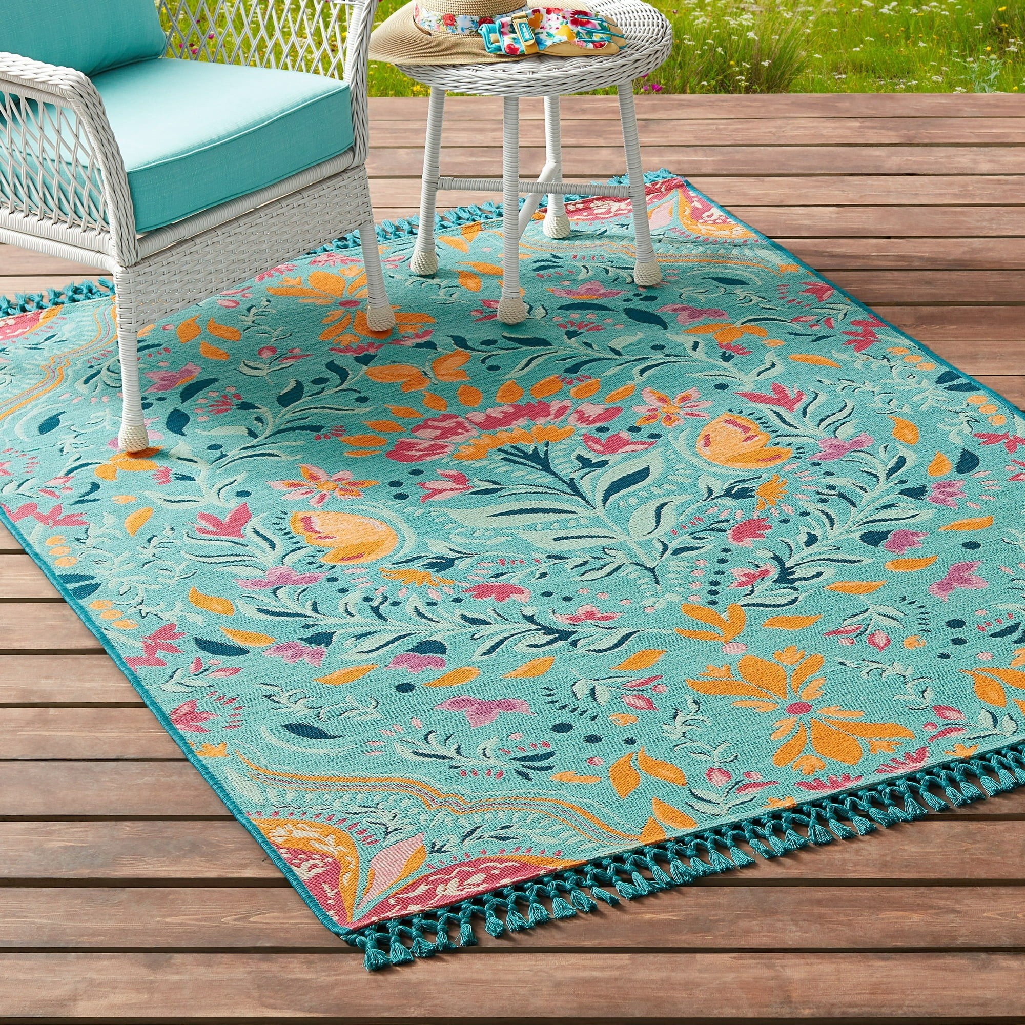 the turquoise rug with yellow and pink accents and fringe on a deck