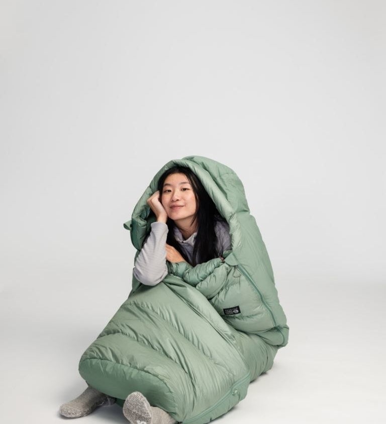 model in sage green sleeping bag with a hood and a zippered foot box