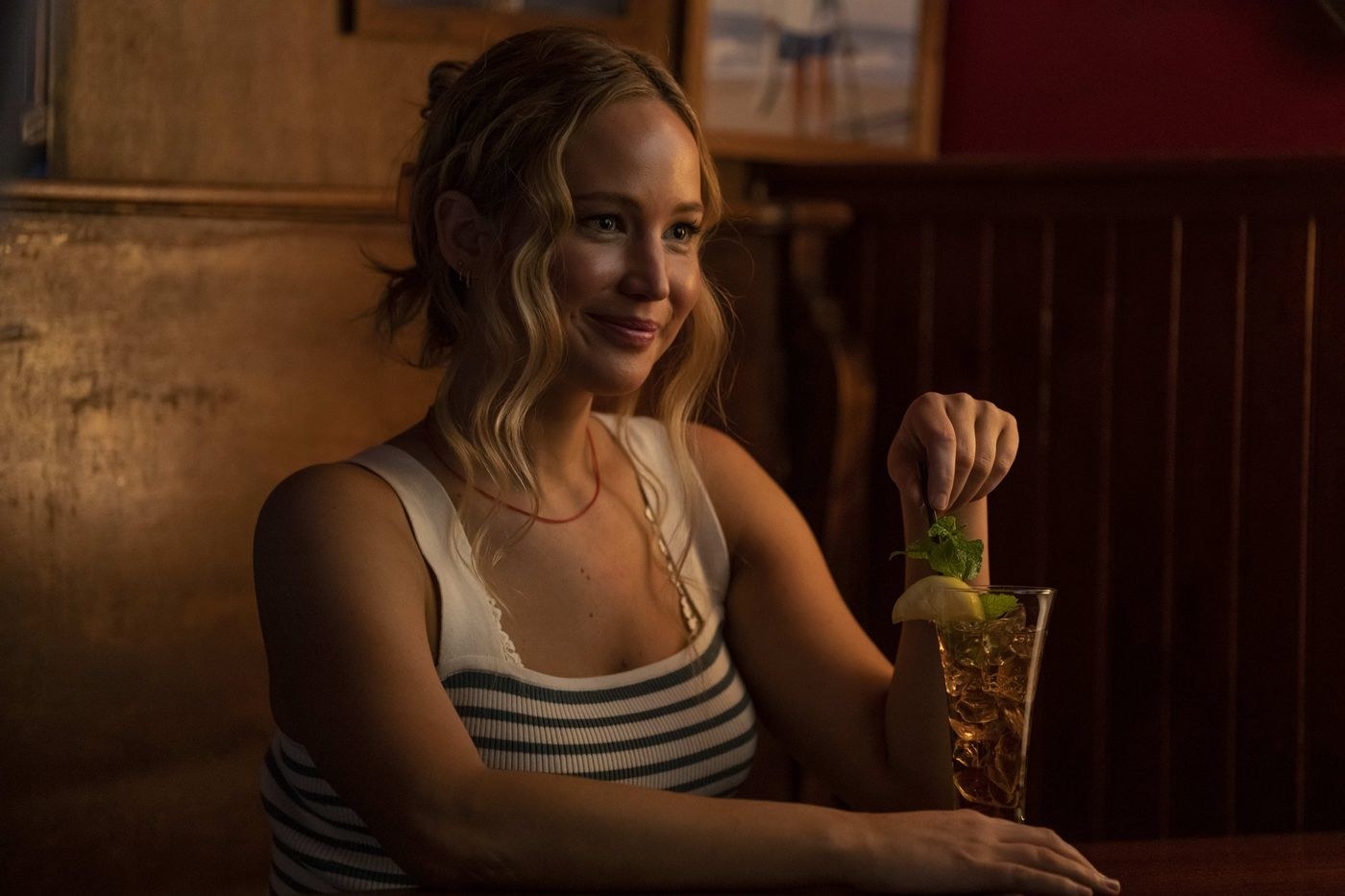 Close-up of Jennifer smiling and sitting in a dining booth with a drink in front of her