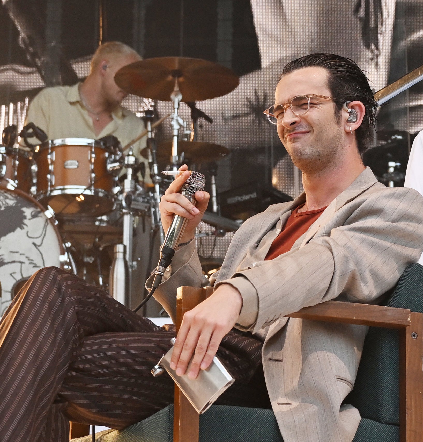 Close-up of Matty sitting down and holding a microphone and a flask