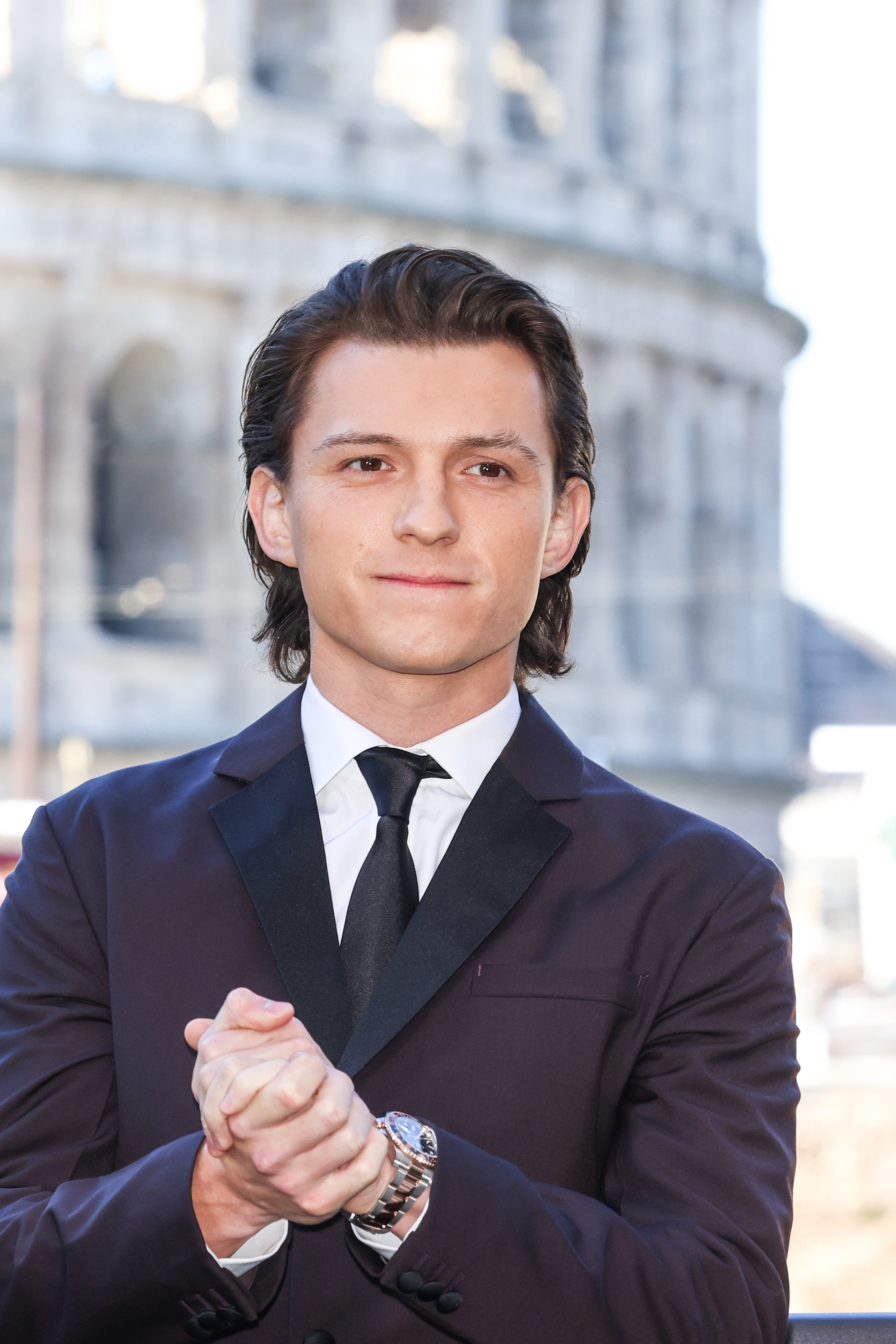 Close-up of Tom in a suit and tie and pressing his hands together